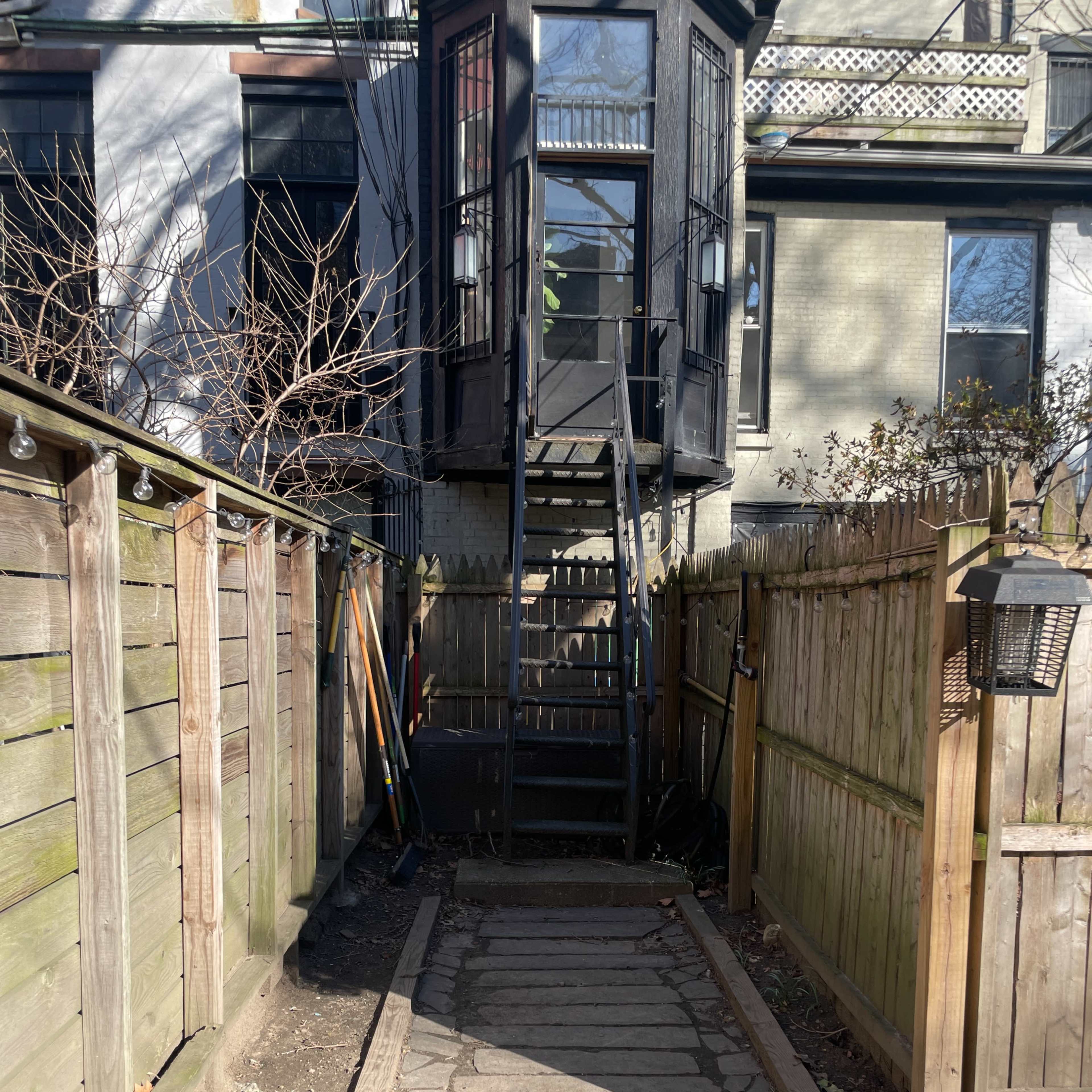 A narrow path leads through a yard toward a stairway enclosed by a black structure at the back.