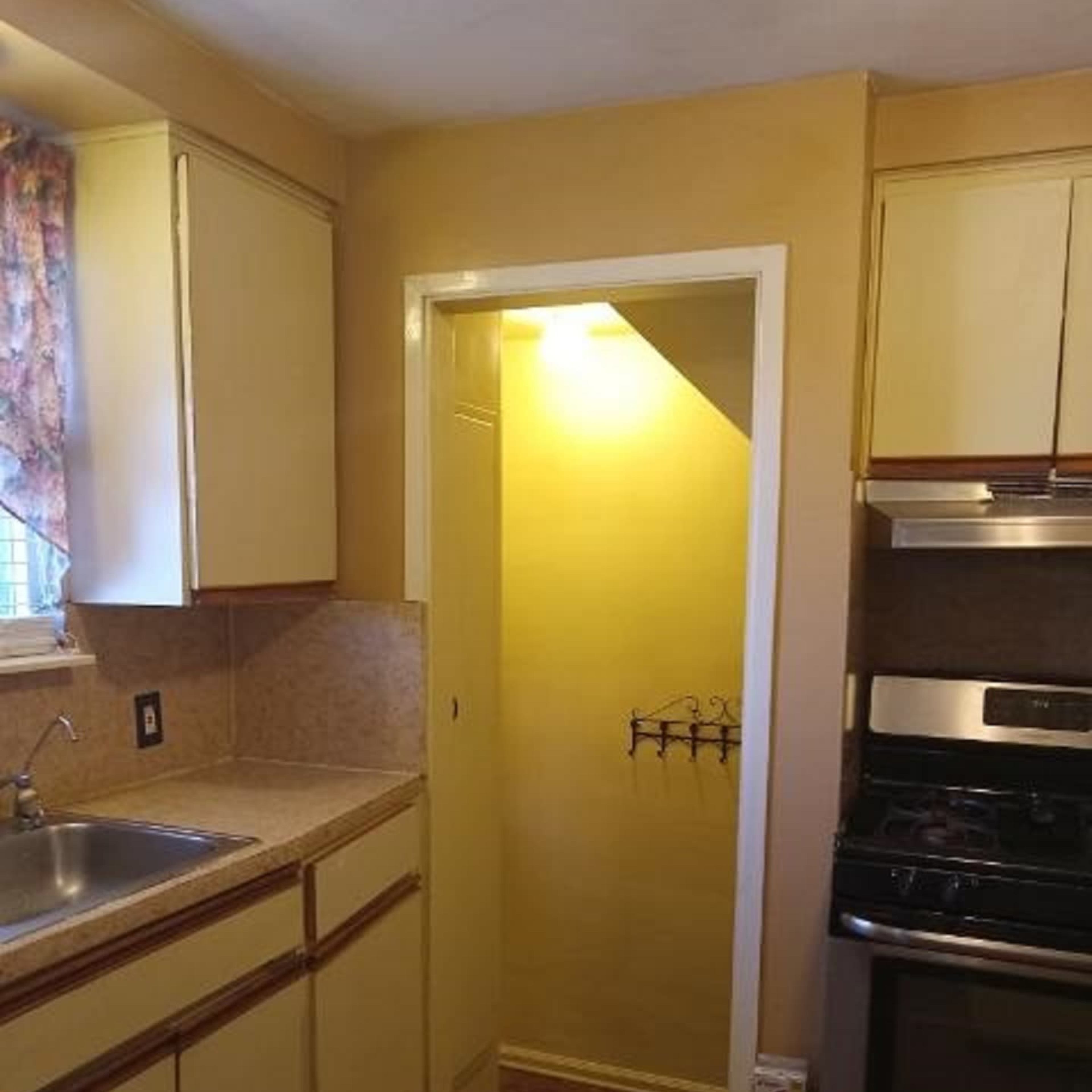 A small kitchen with yellow walls, a sink, and a door leading to a closet or pantry area.