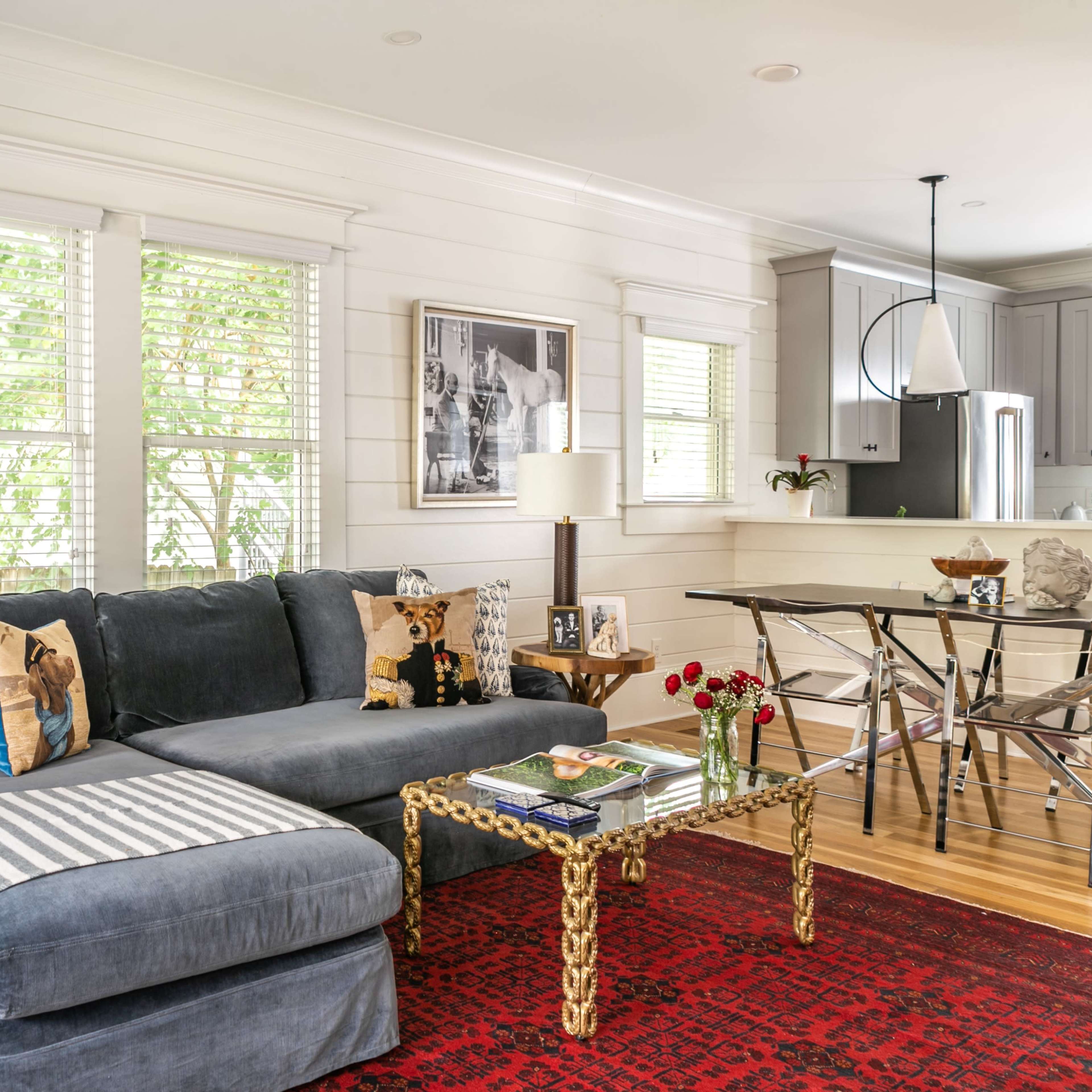A modern living room with a dark sectional sofa, a patterned area rug, a coffee table, and large windows letting in natural light.