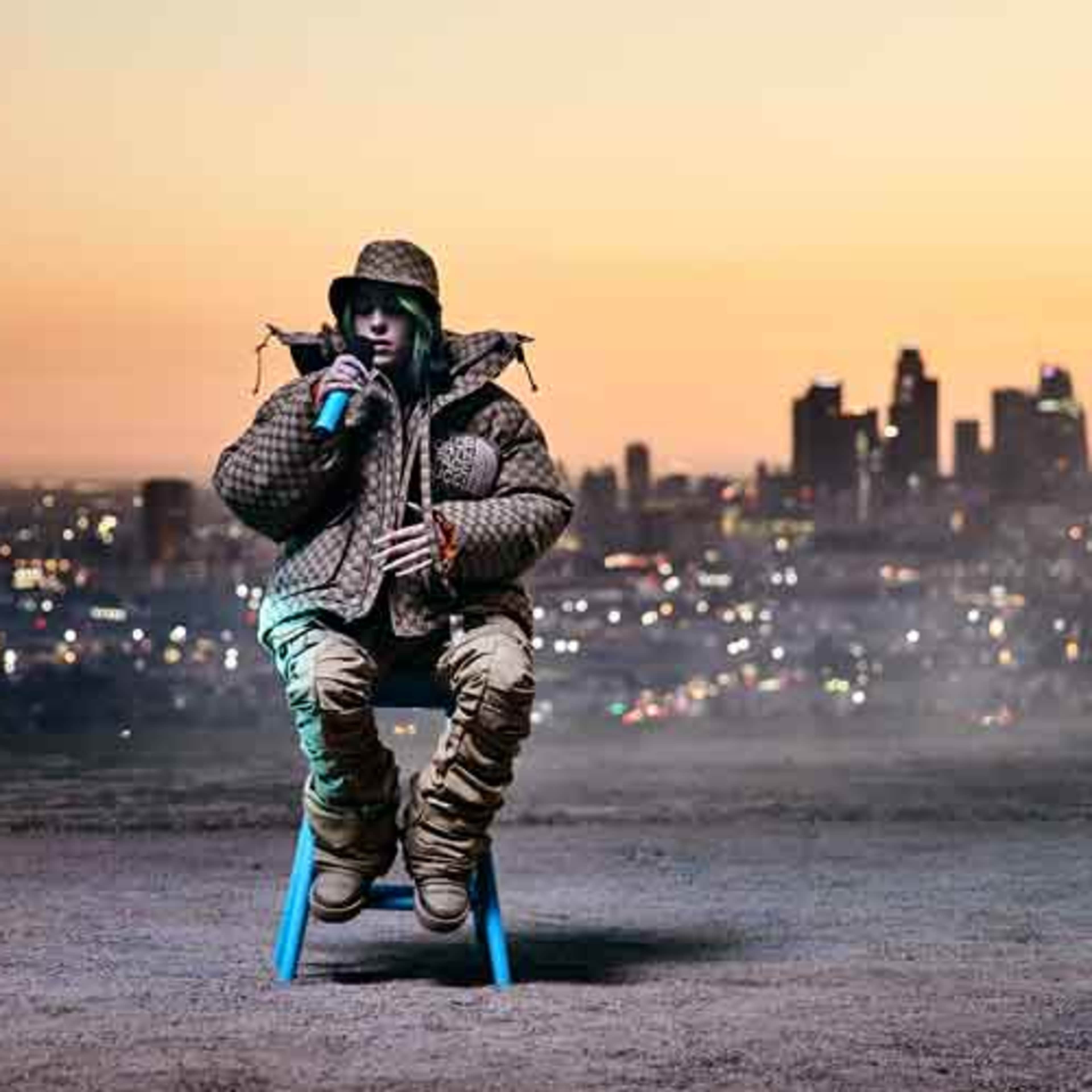 A person wearing a patterned coat and khaki pants sits on a blue chair against a city skyline at sunset.