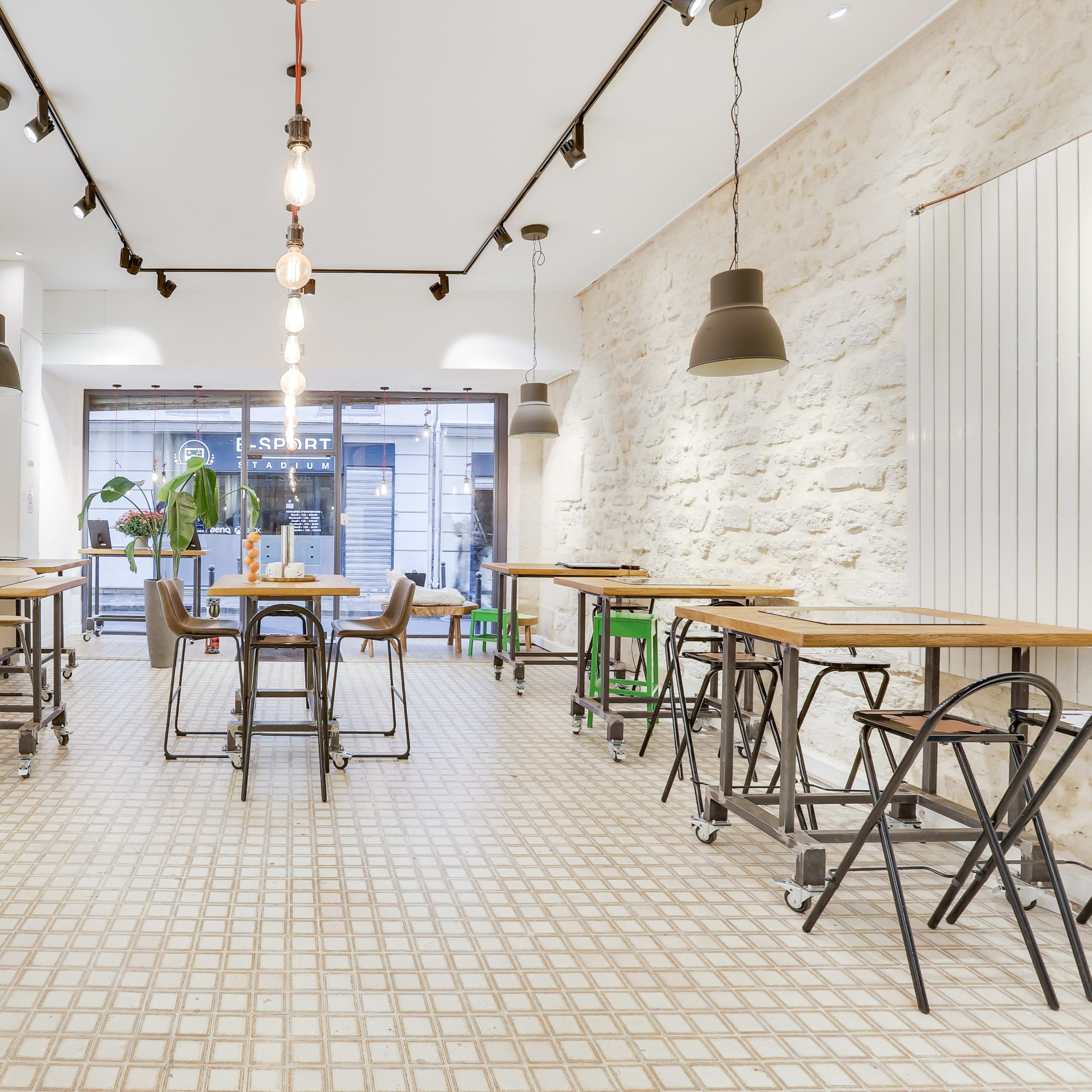 A modern café interior with wooden tables and metal chairs, featuring a tiled floor and pendant lighting.