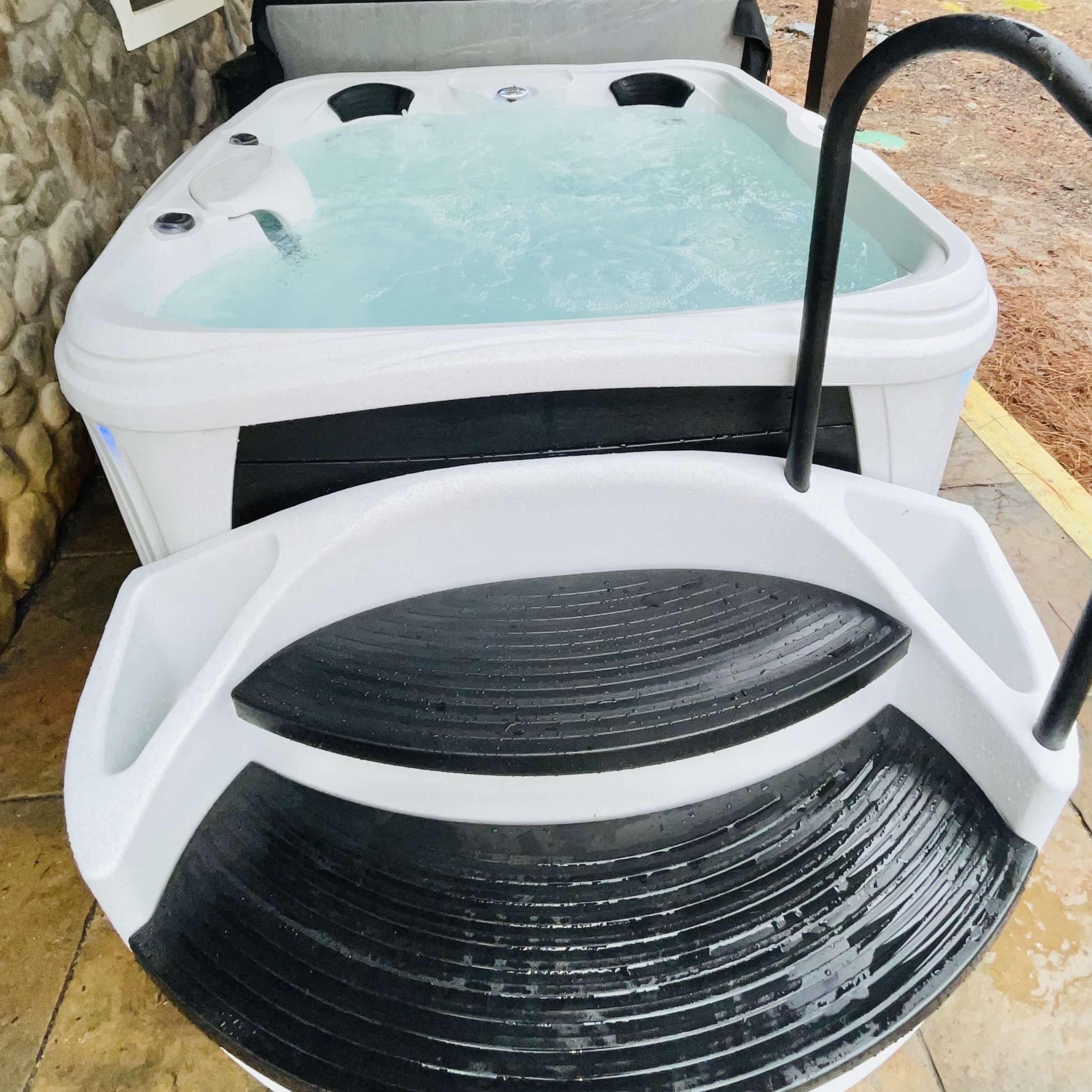 A hot tub with water inside, accompanied by a set of black steps leading up to it.