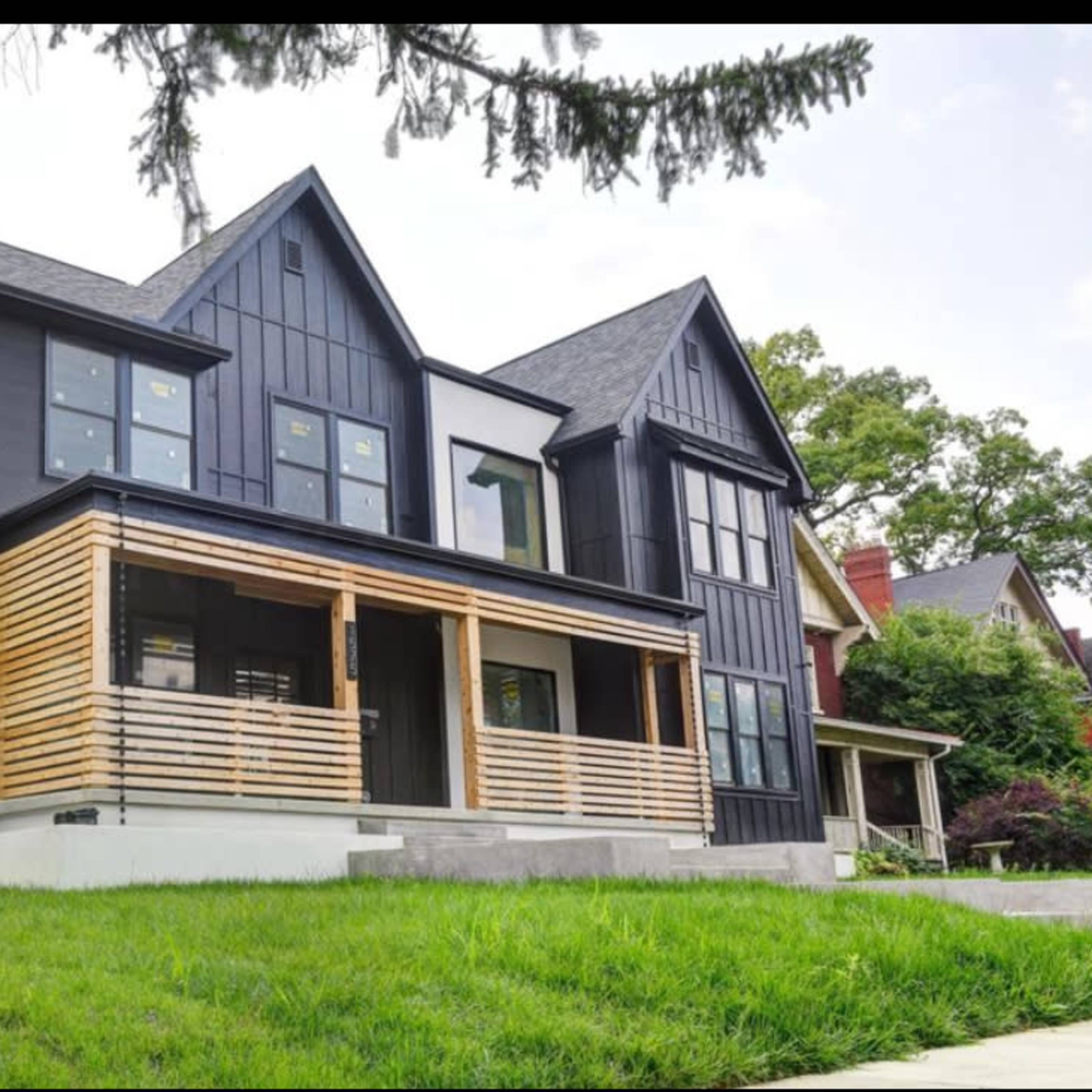 A modern black house with wooden accents and a front porch is surrounded by a green lawn.