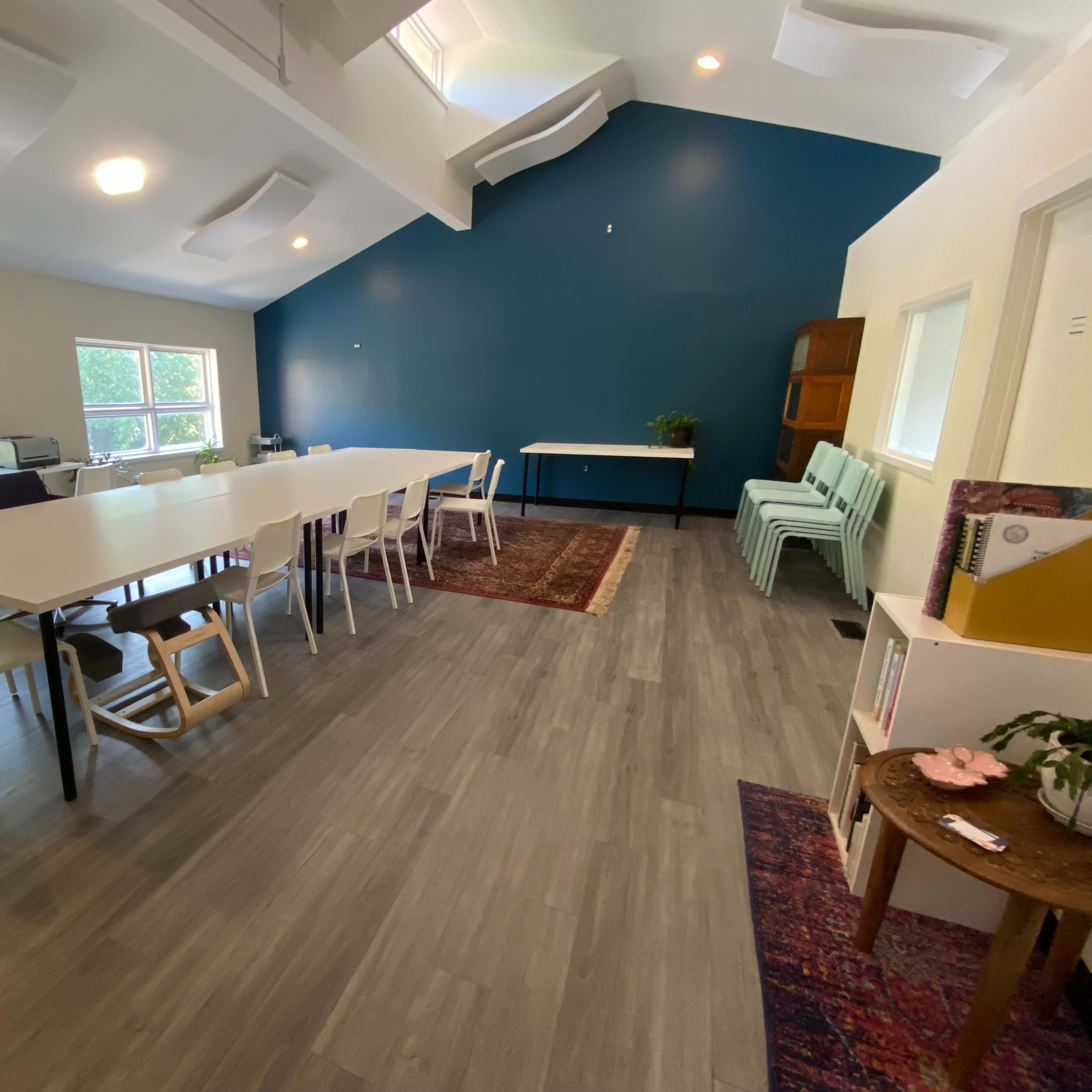 A bright, spacious meeting room with a long white table, light green chairs, and blue accent wall.
