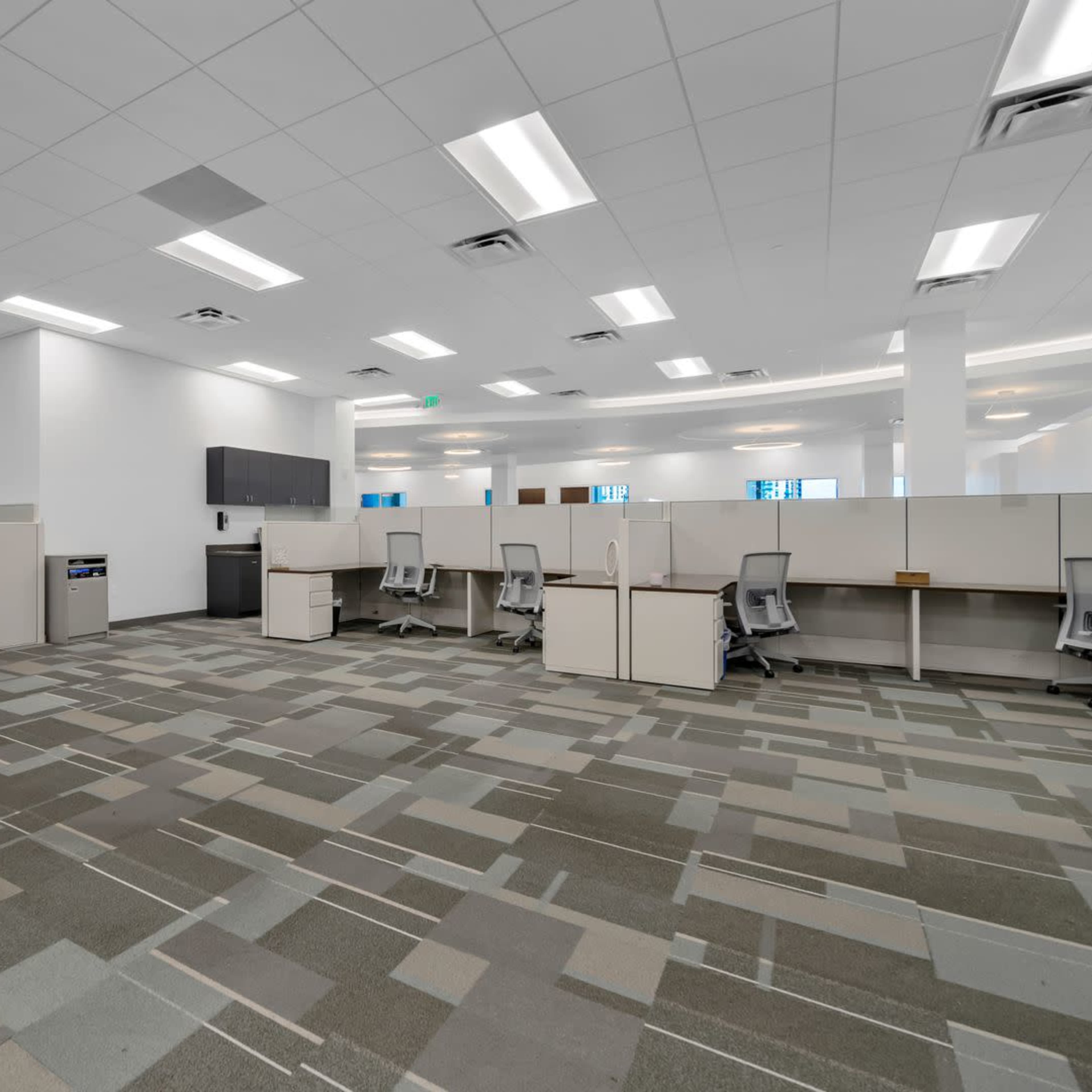 A spacious, empty office area with cubicles, modern furnishings, and a patterned carpet.
