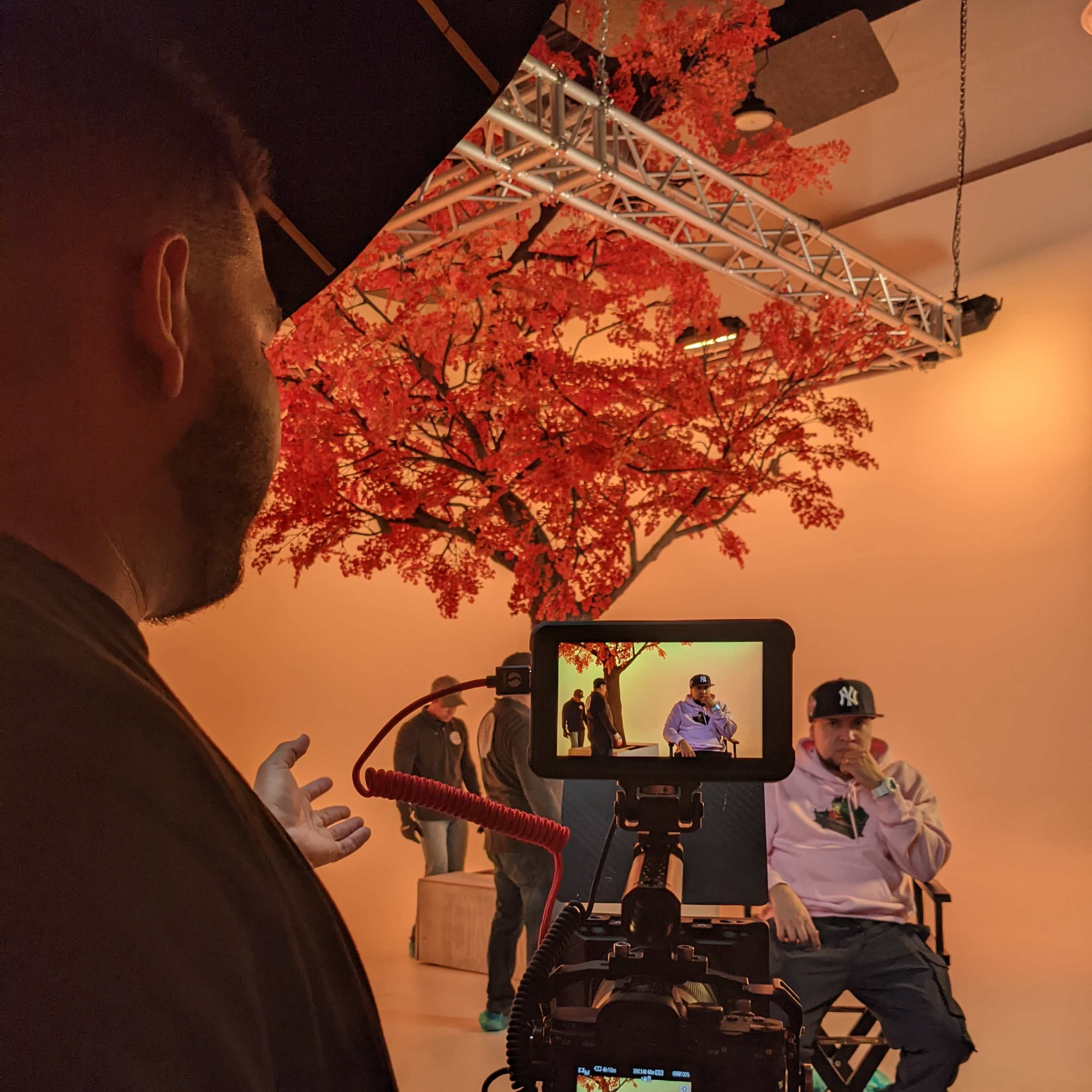 A photographer captures an individual seated in front of a large artificial tree in a studio setting.