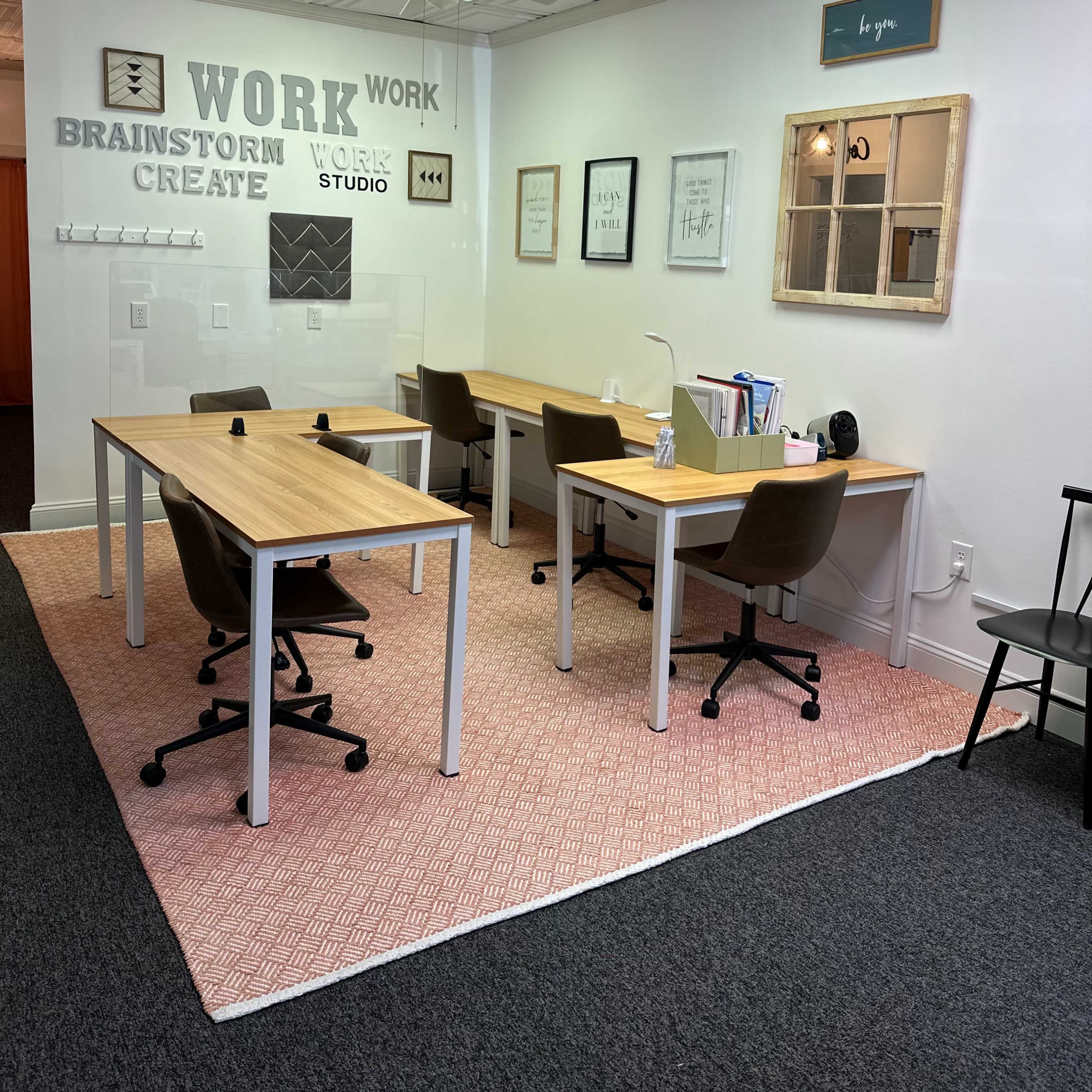 A workspace with two wooden desks and chairs arranged on a patterned rug, complemented by wall art and a mirror.