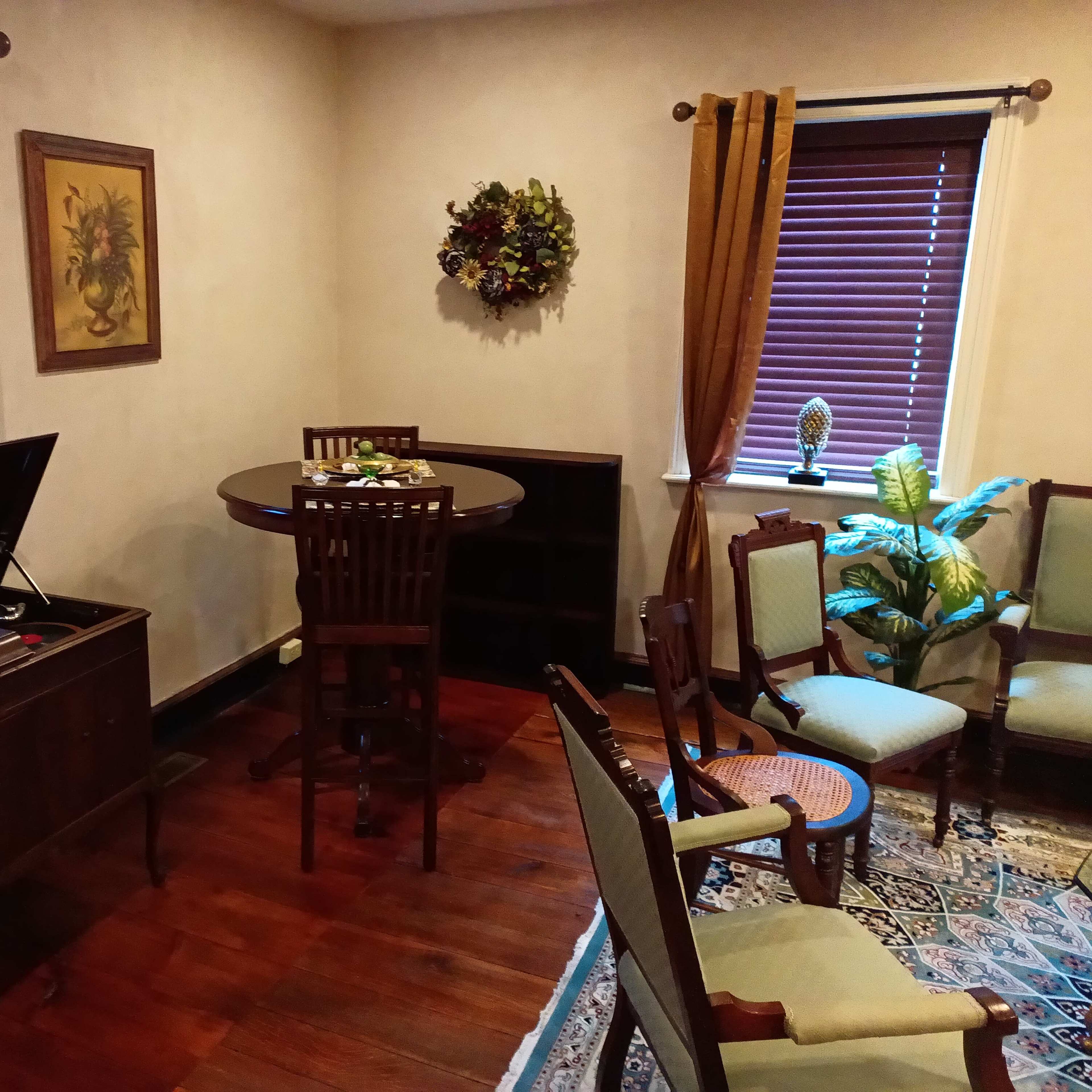 A room furnished with a round table and chairs, a decorative wall hanging, and a record player on a cabinet.