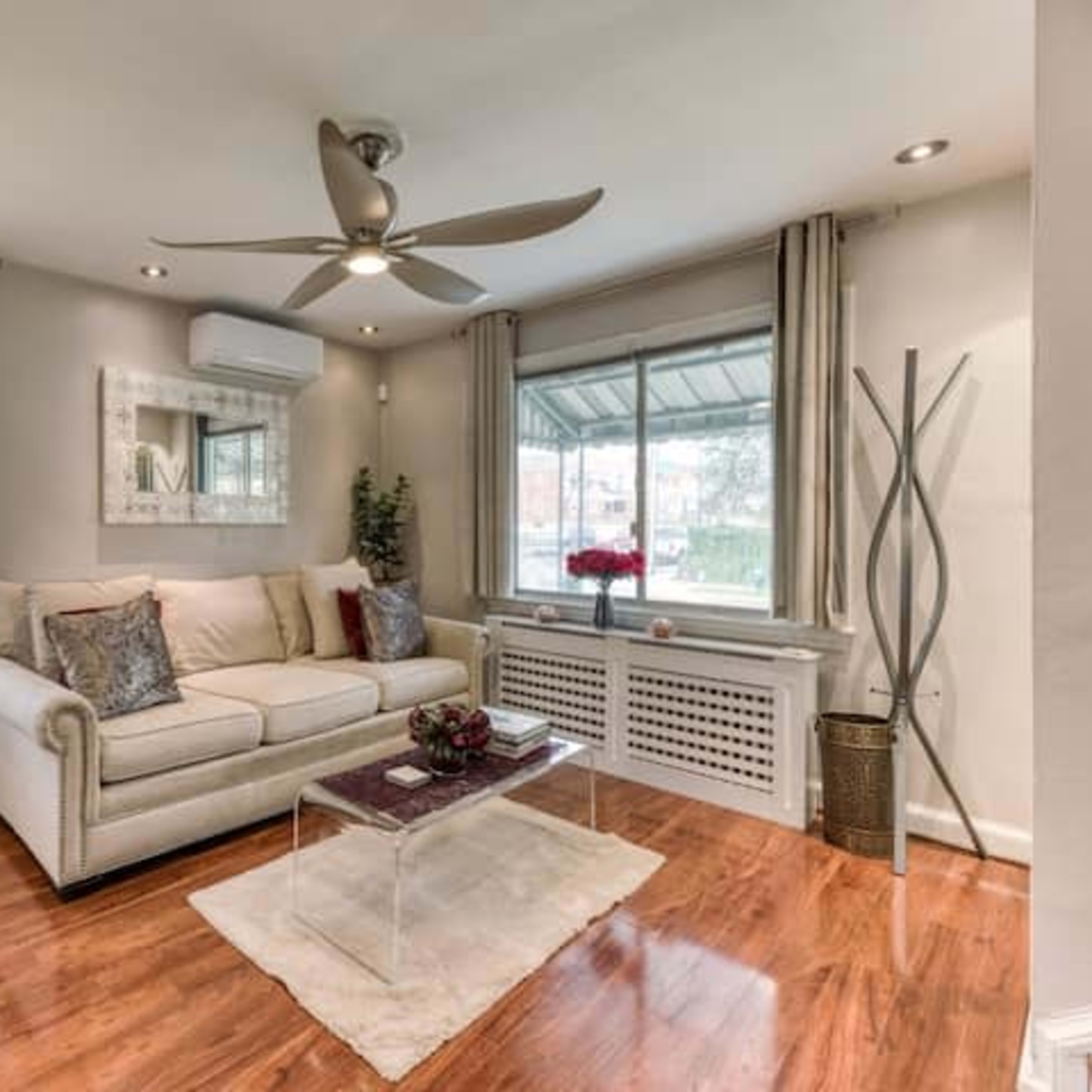 A living room with a beige sofa, a clear coffee table, and large windows allowing natural light to enter.