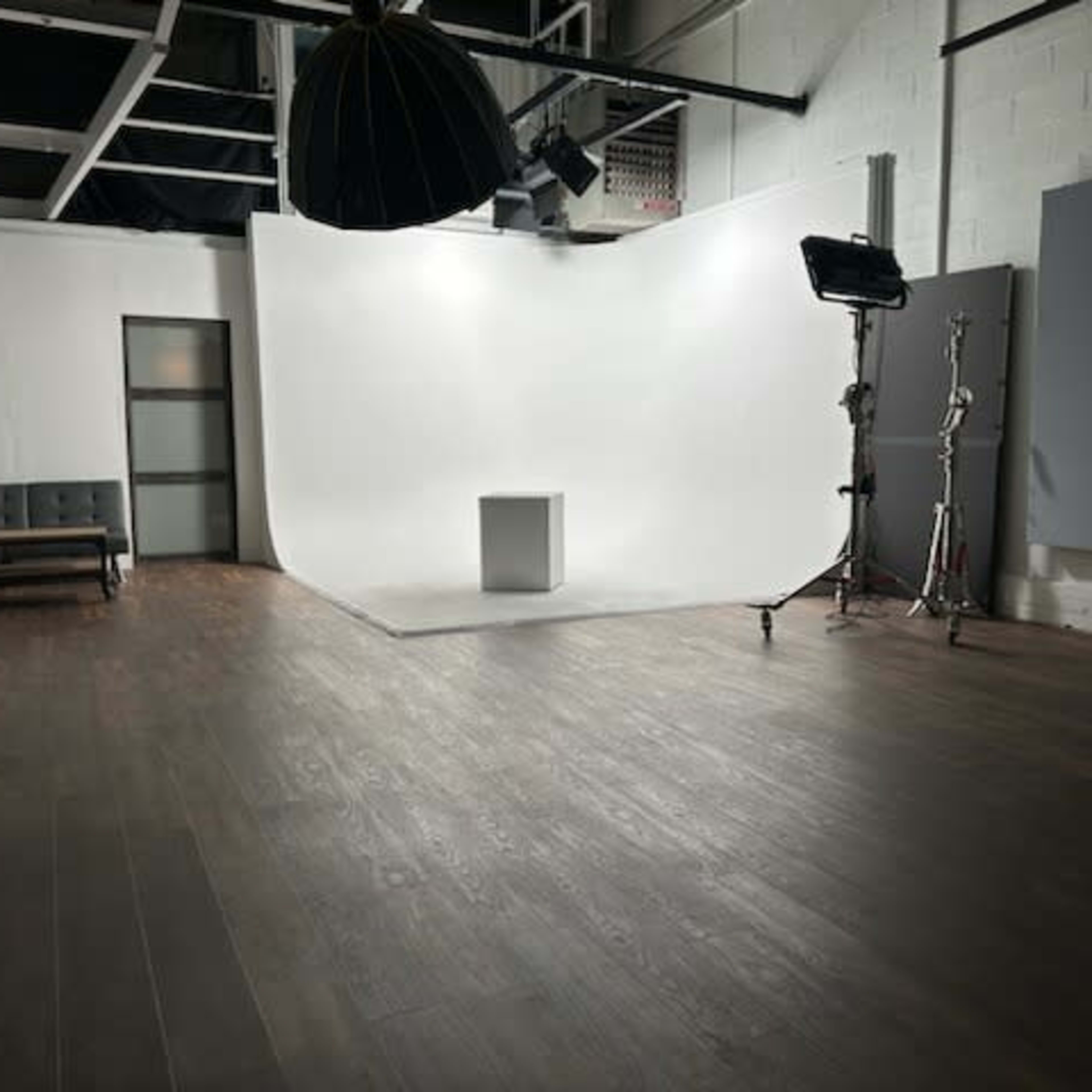 A photography studio features a white backdrop, a single pedestal, and soft lighting equipment on display.