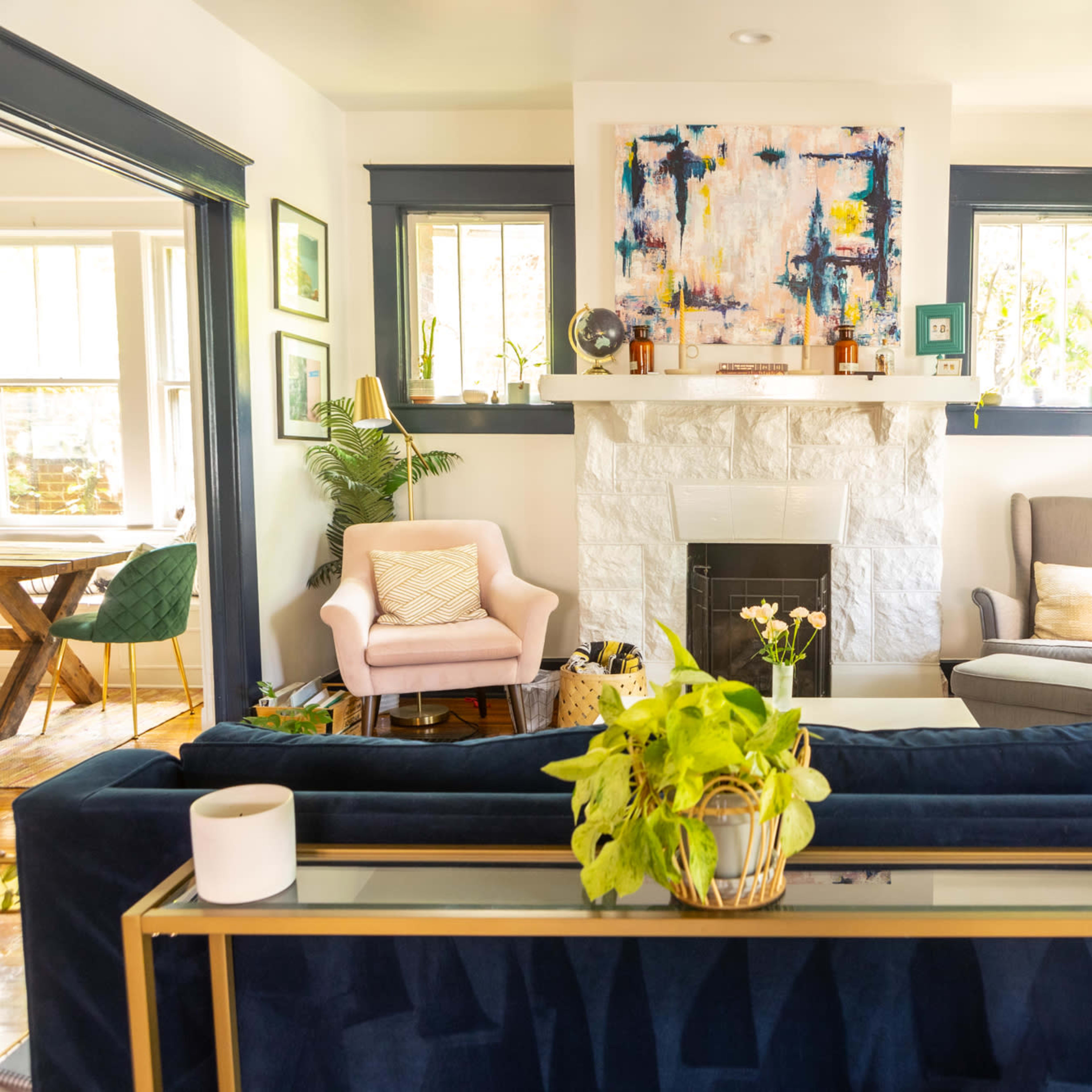 A bright living room featuring a navy blue sofa, two armchairs, a white stone fireplace, and colorful artwork above the mantel.