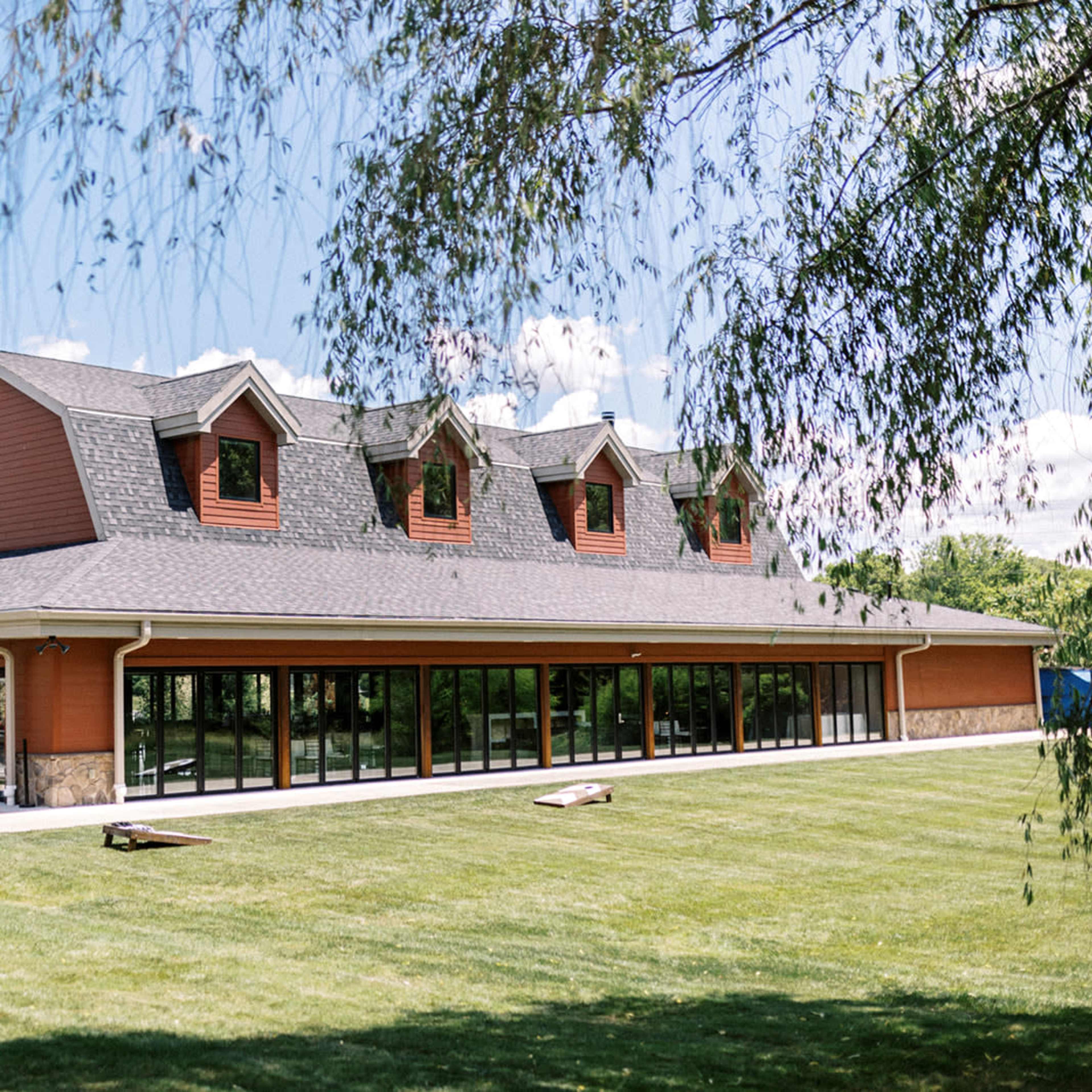 A large, modern building with multiple peaked roofs and extensive glass windows, situated on a grassy area under a blue sky.