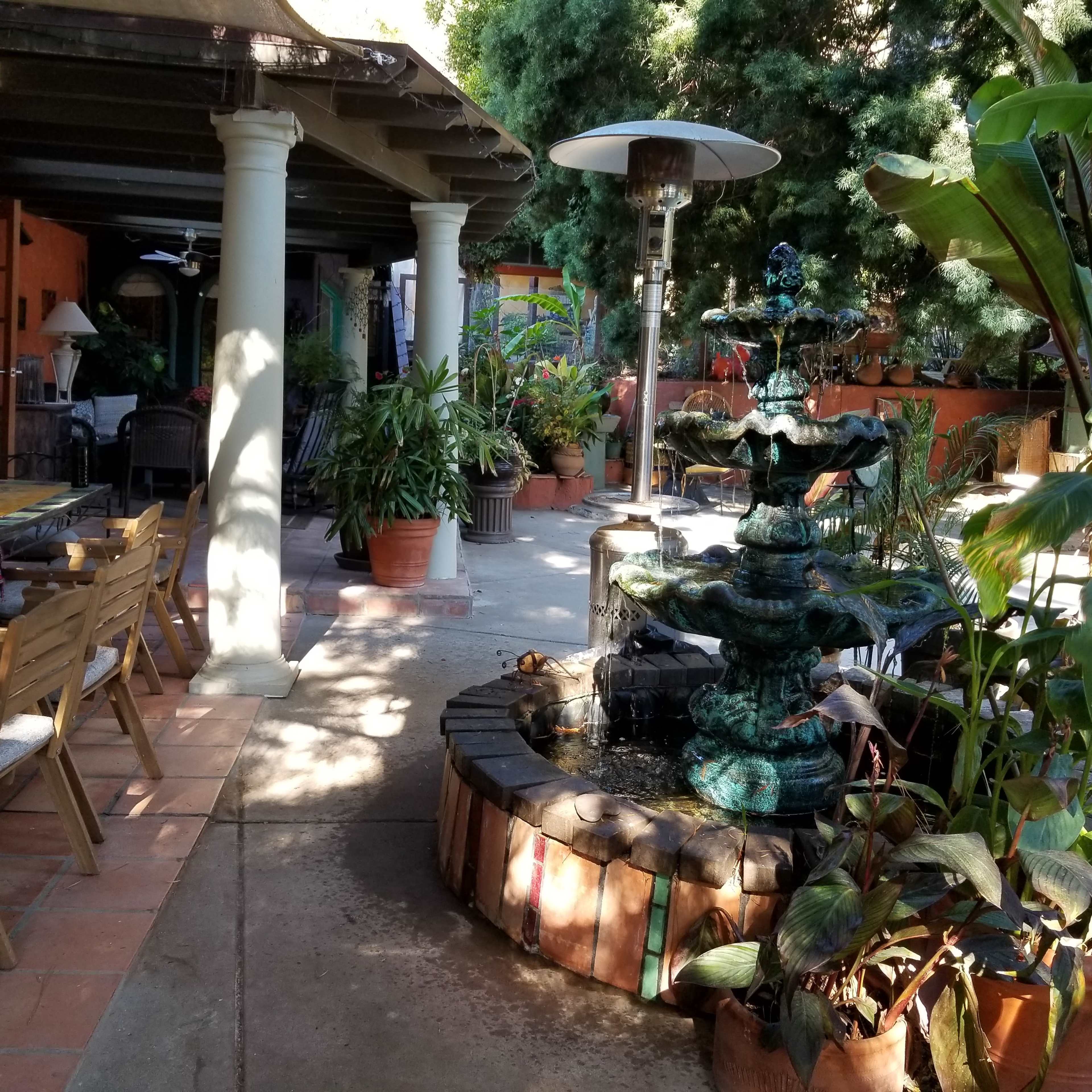 A courtyard with a tiered fountain surrounded by potted plants, tables, and chairs under a covered patio.