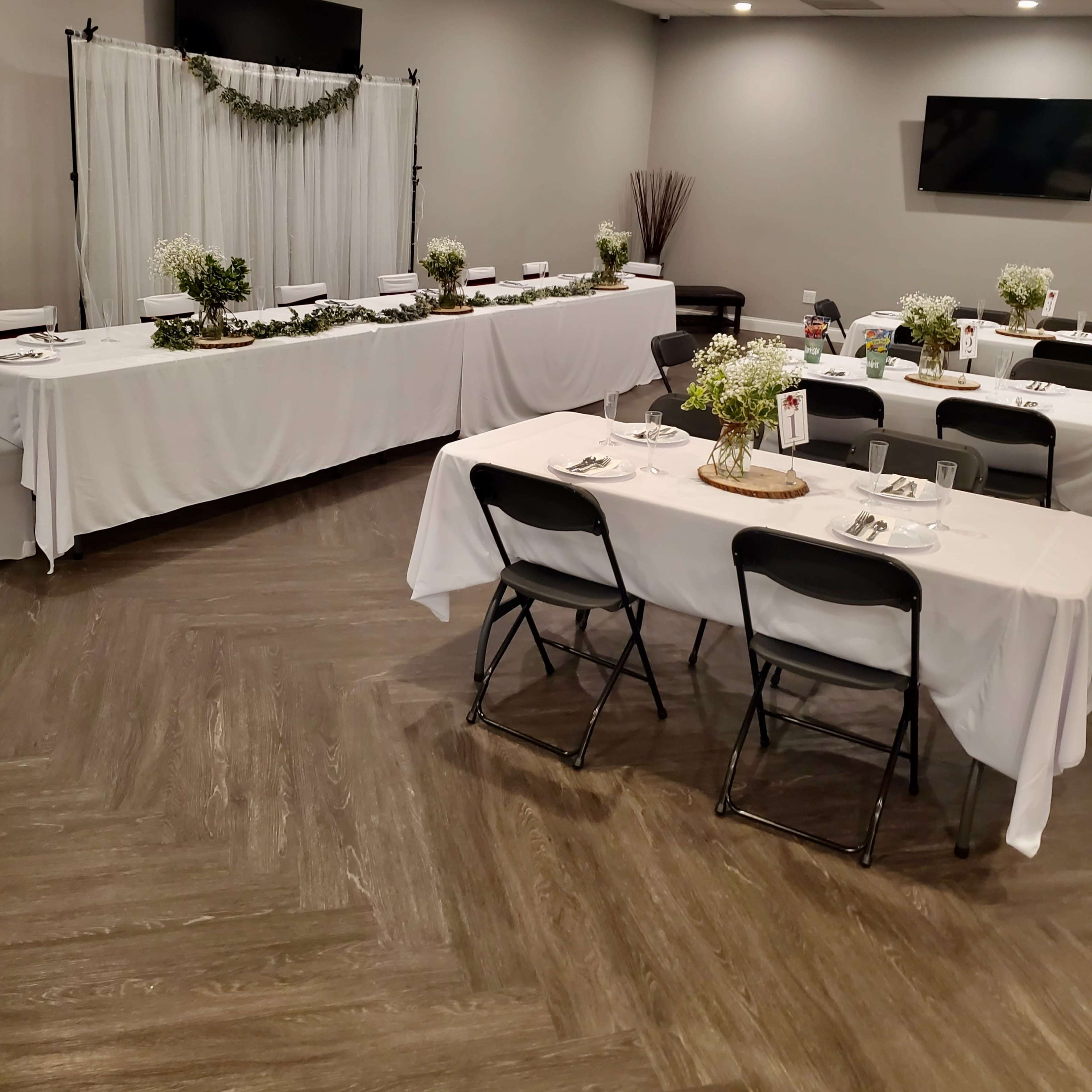 A banquet room is set up with white tablecloths, chairs, and decor, including small floral centerpieces.