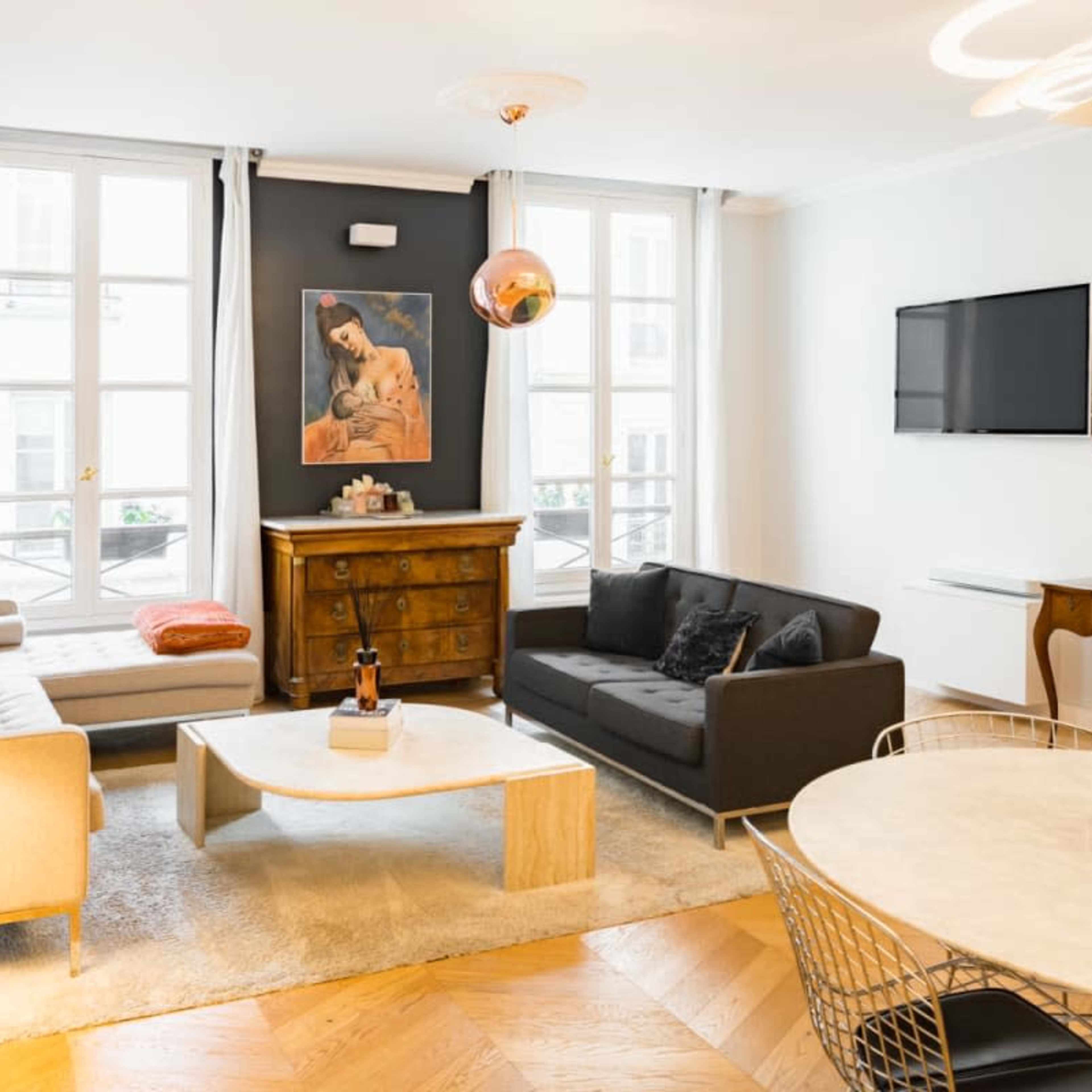 The living room features two sofas, a coffee table, a dining area with round table, and large windows letting in natural light.