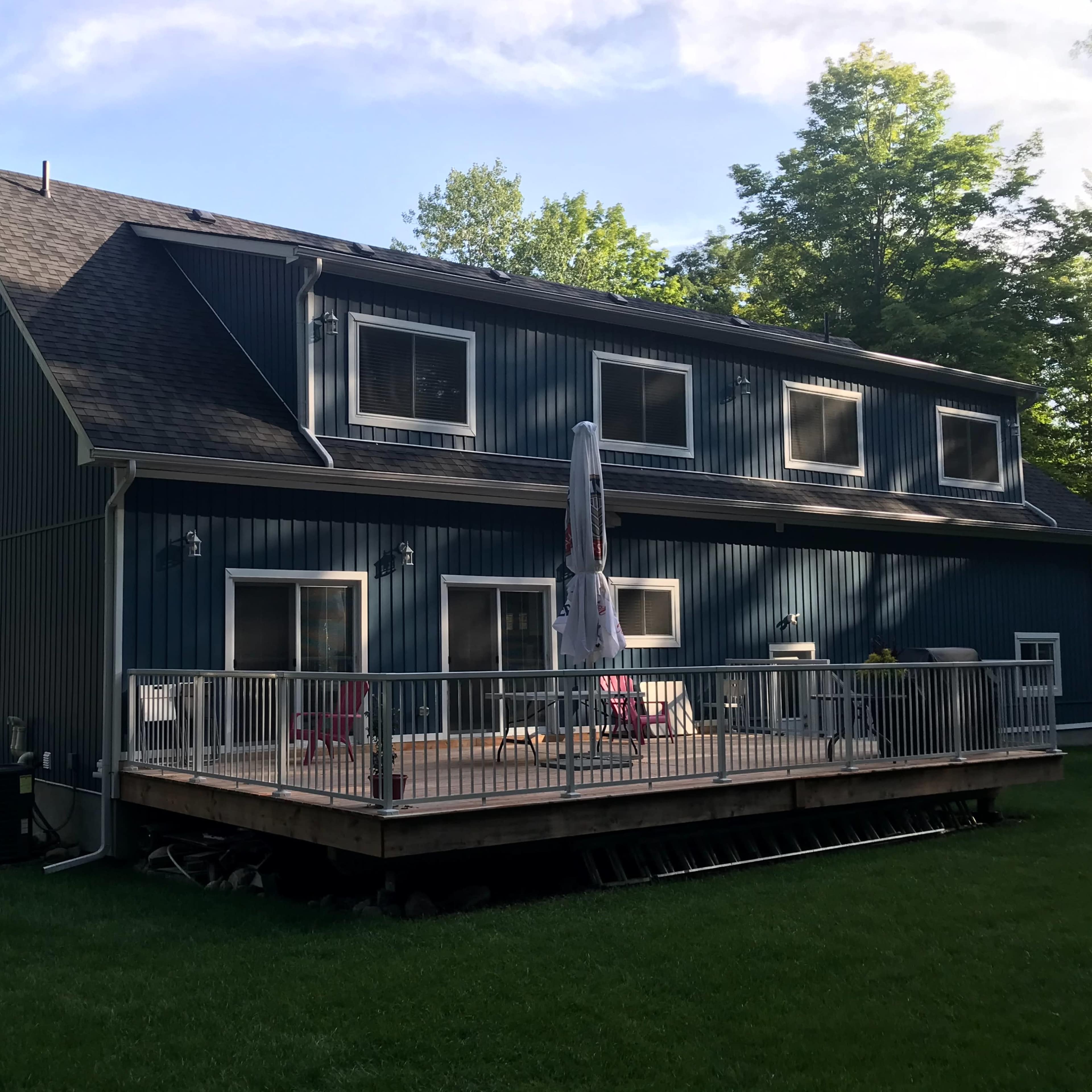 A blue two-story house sits behind a wooden deck surrounded by trees.