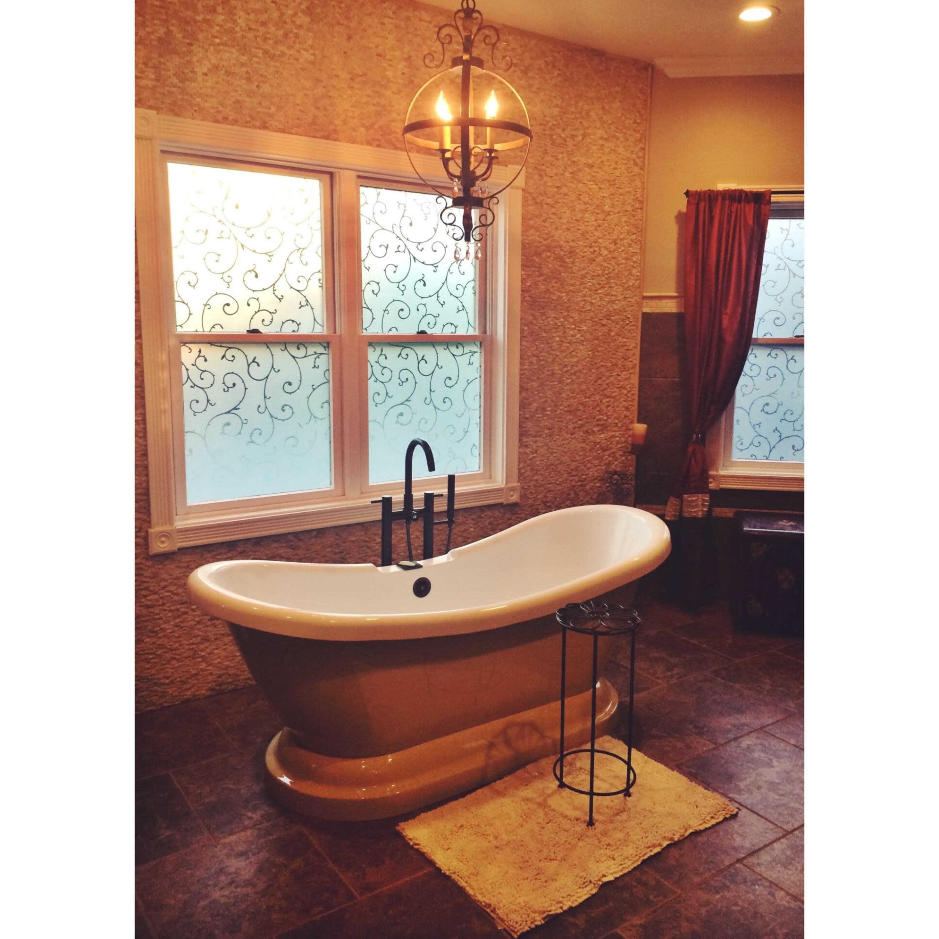 A spacious bathroom featuring a freestanding bathtub, a small side table, and decorative windows with patterned glass.