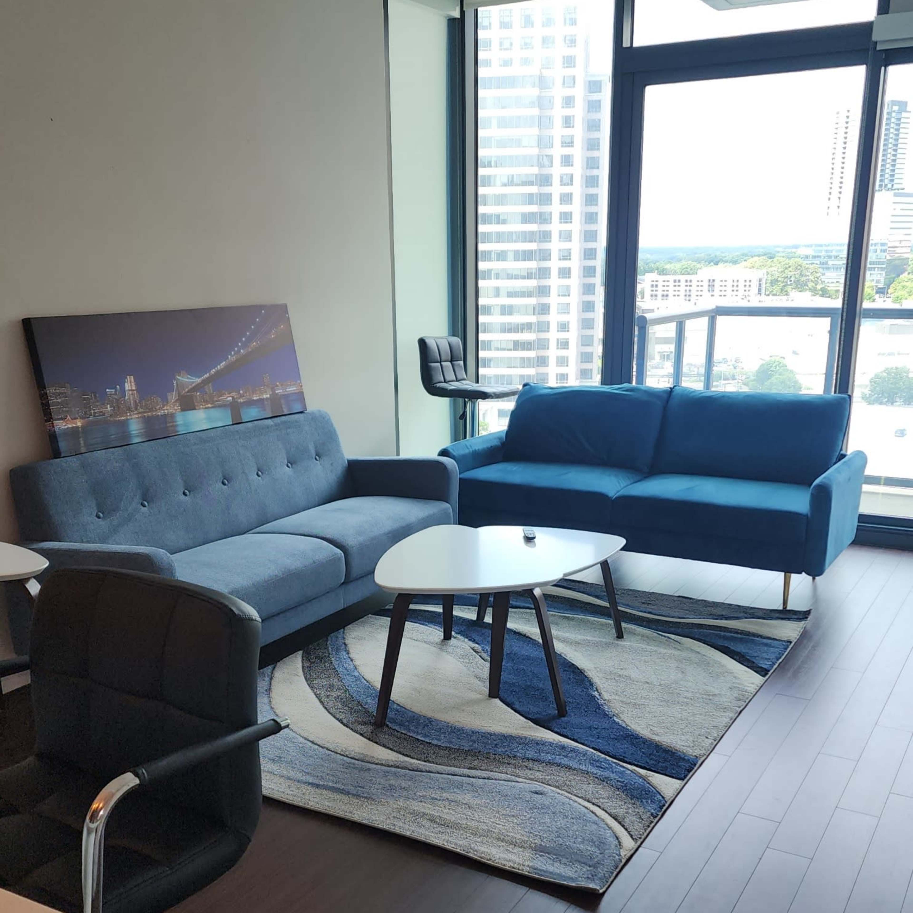 A modern living room with a blue sofa, a gray couch, a circular coffee table, and a large window overlooking a cityscape.