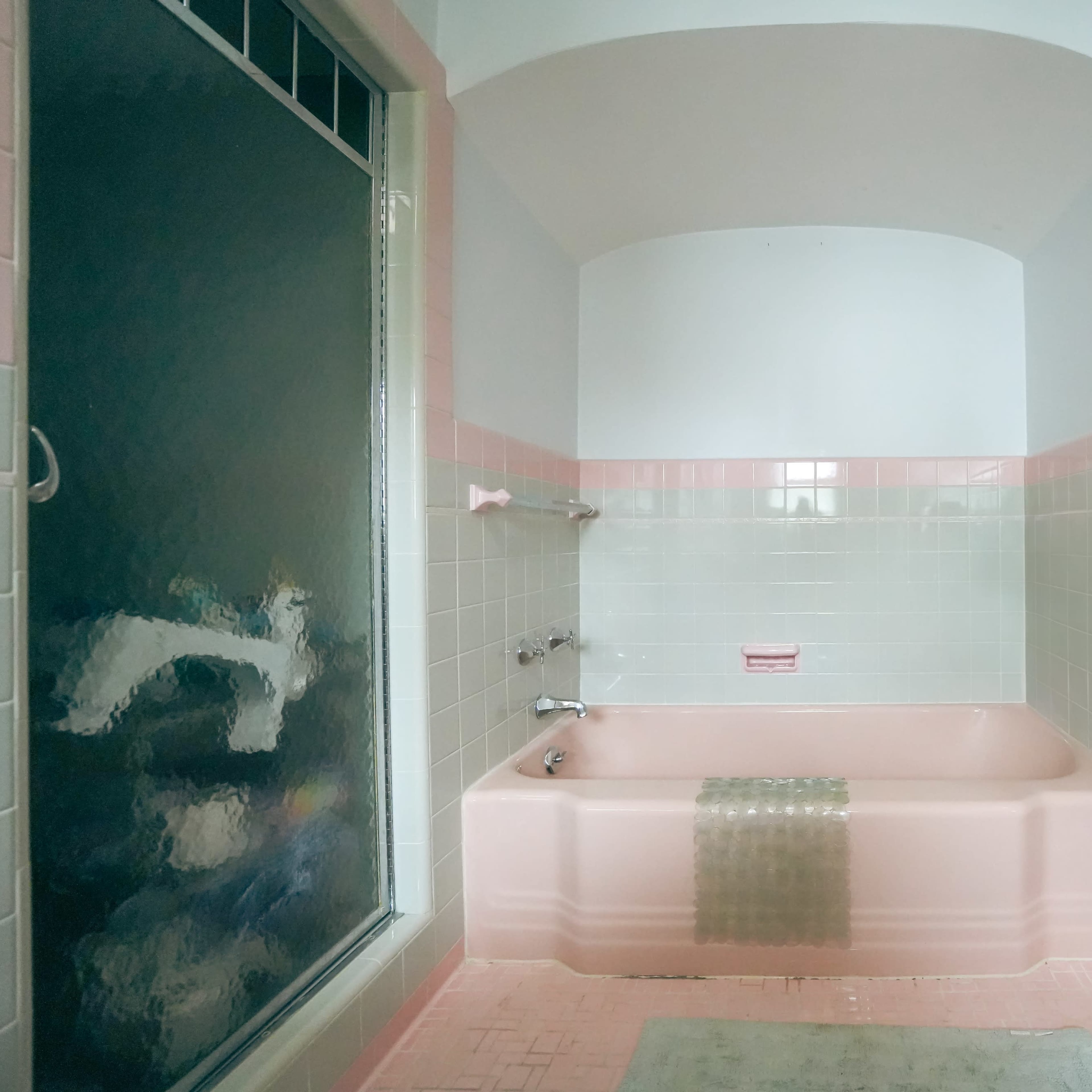 A bathroom with a pink bathtub, pink walls, and a glass shower enclosure.