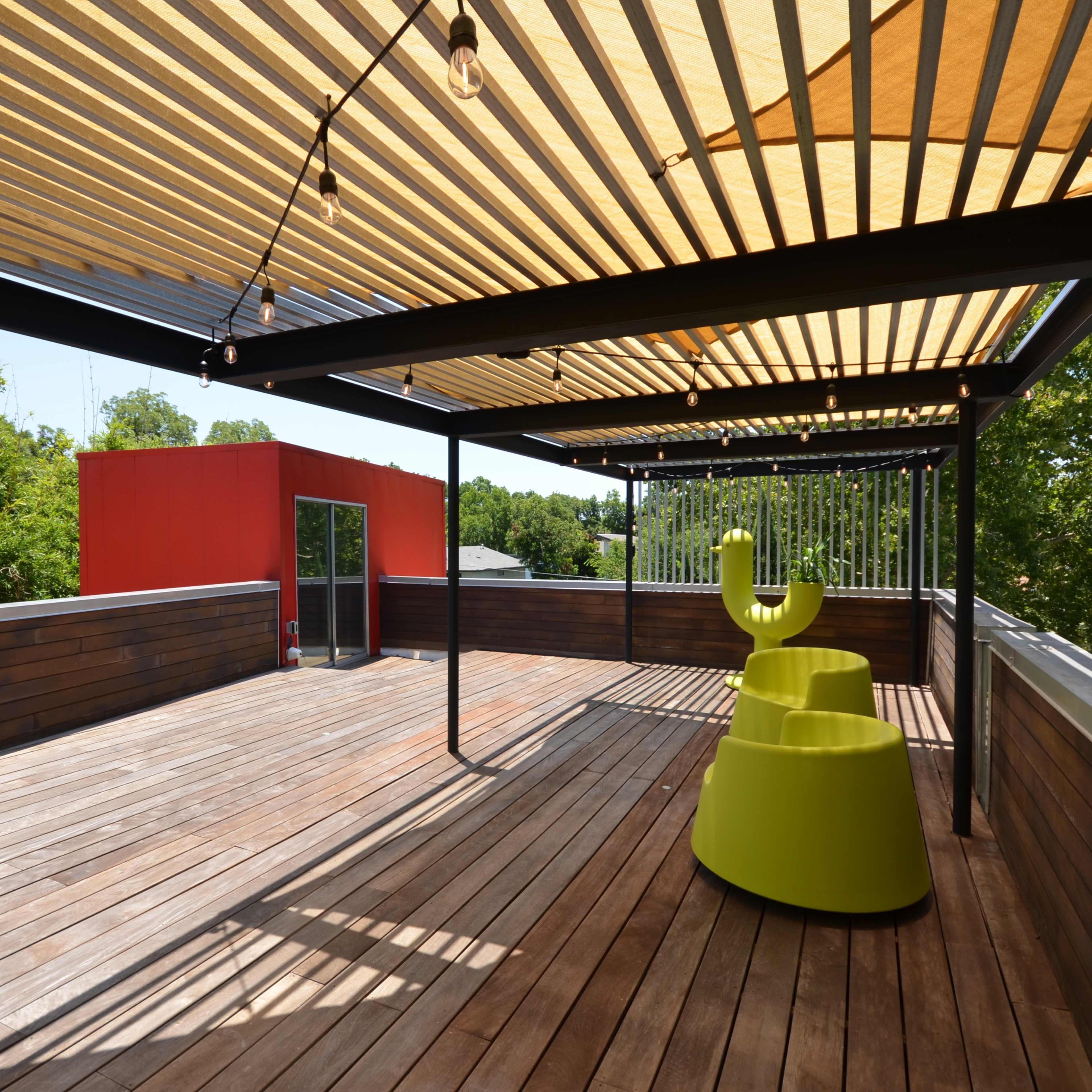 A wooden terrace features yellow seating under a striped canopy with a red structure in the background.