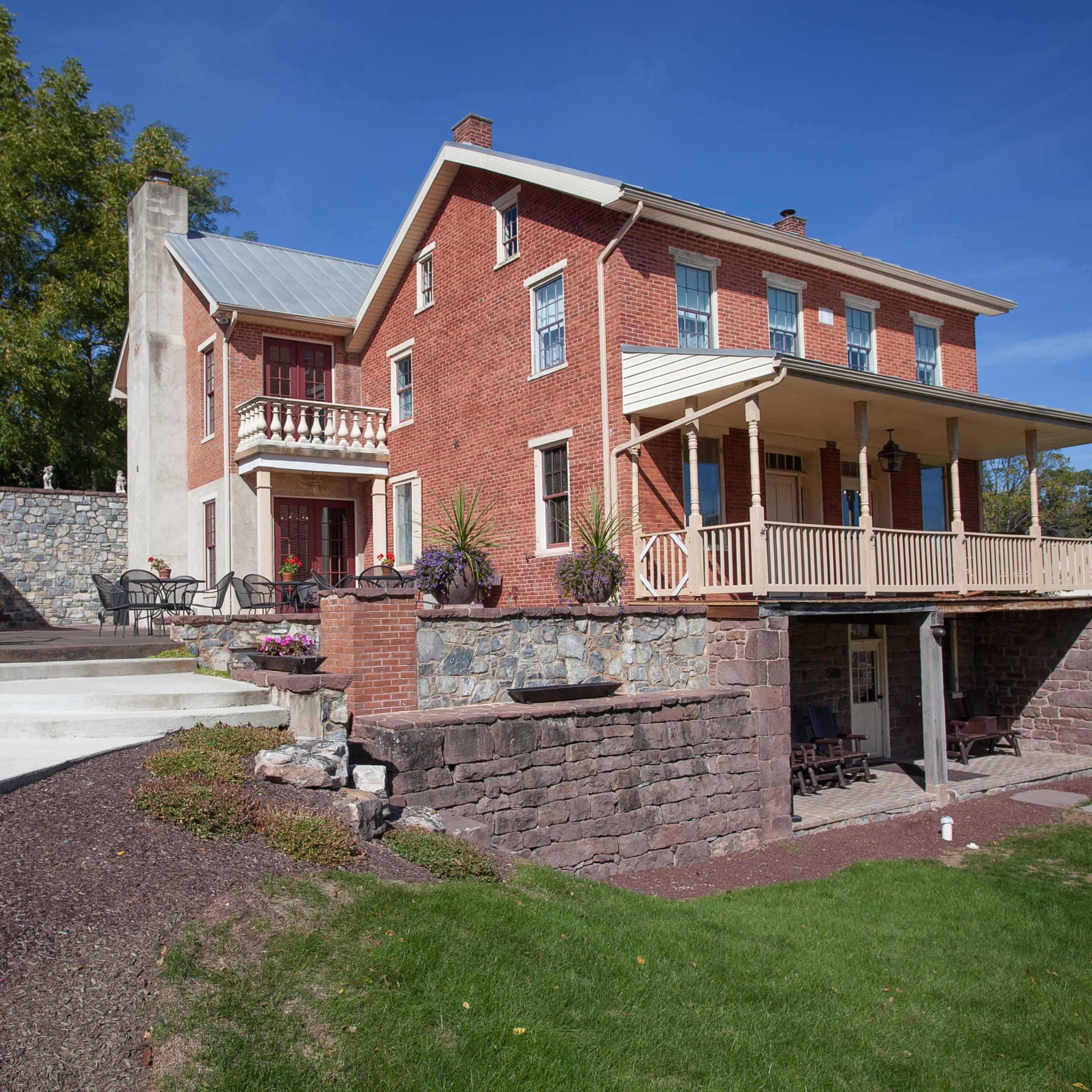A two-story brick house with a porch, surrounded by landscaped gardens and stone pathways.