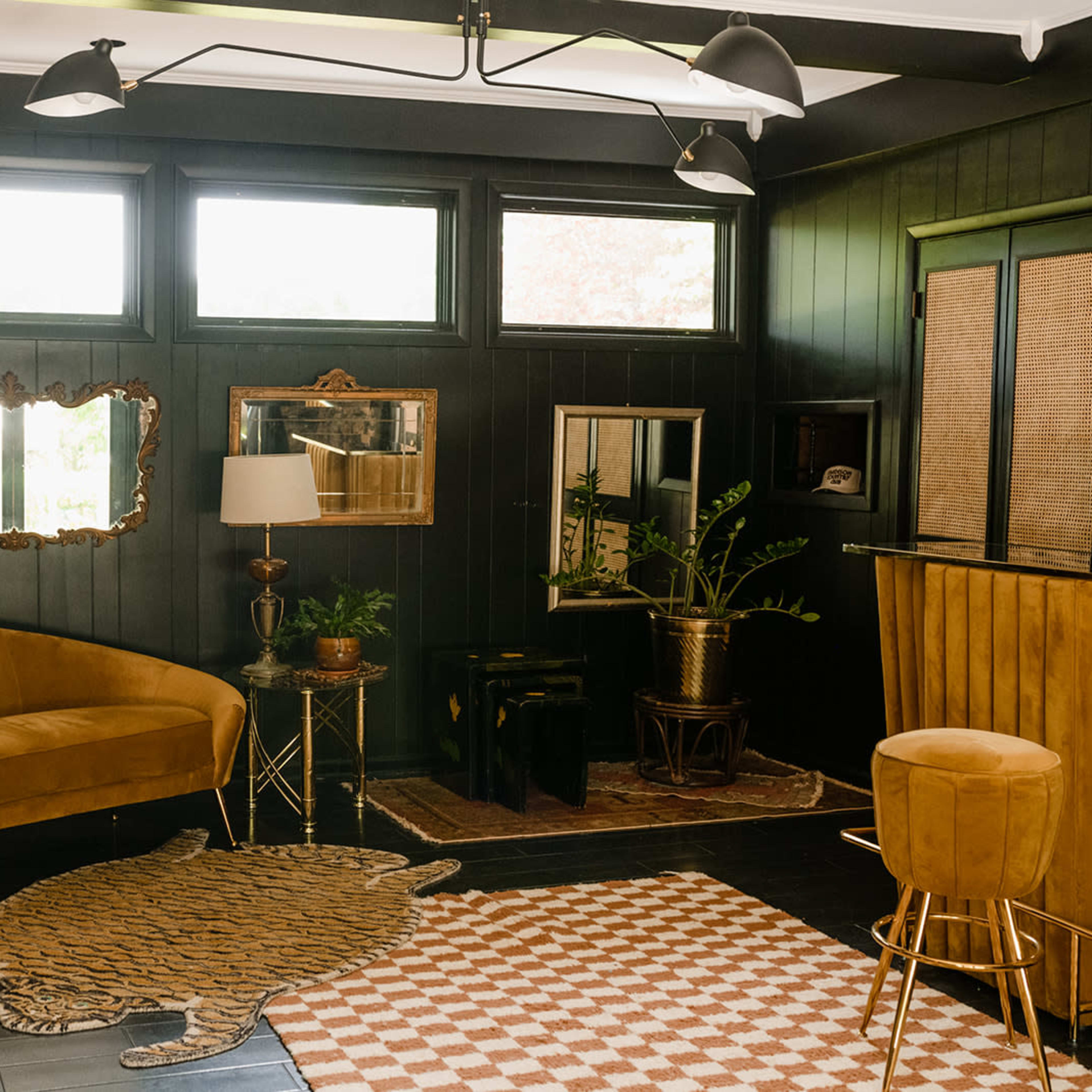 A stylishly decorated room with dark wooden walls, a curved sofa, a rug shaped like a tiger, and several plants, alongside modern lighting fixtures.