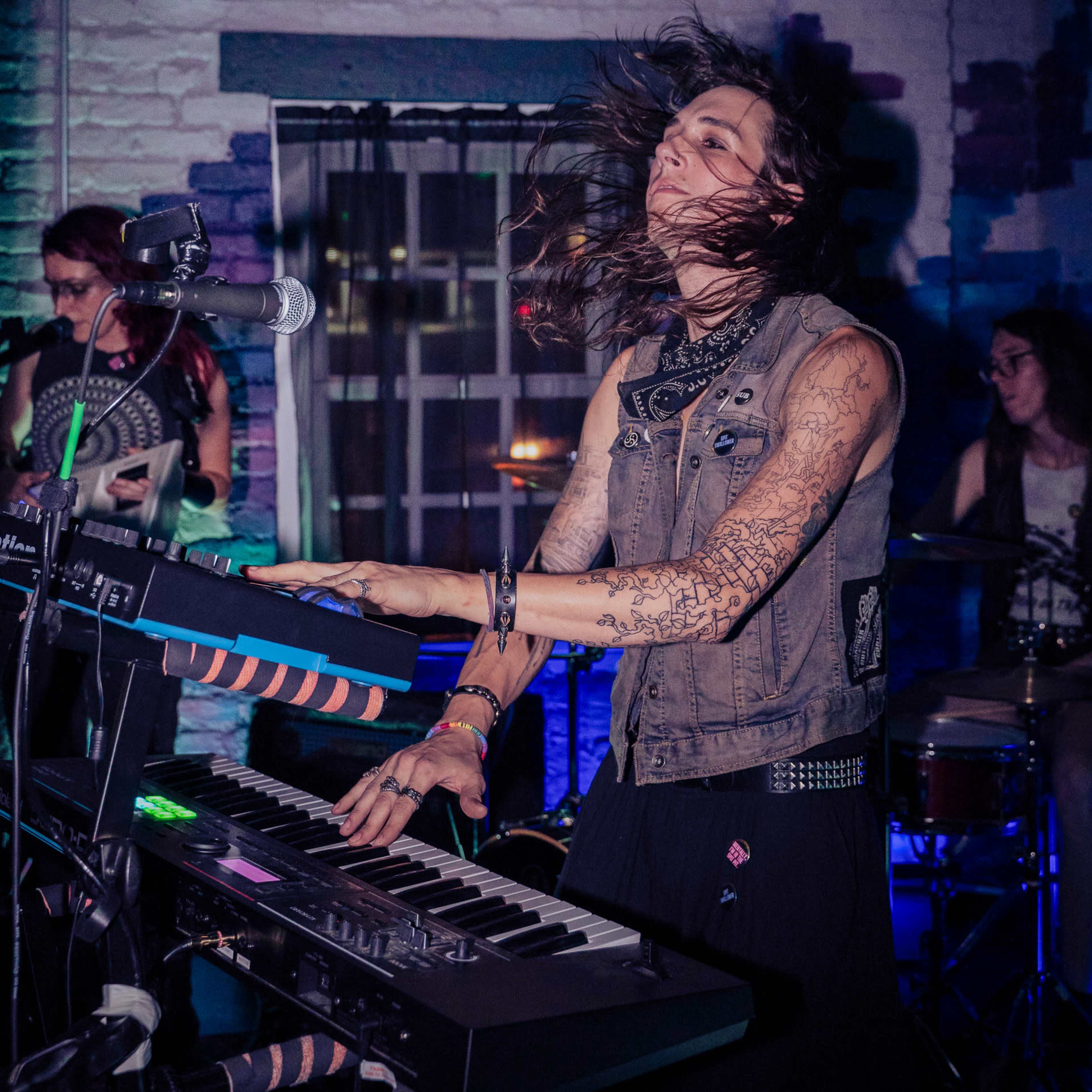 A musician plays a keyboard with long hair flowing as they perform on stage.