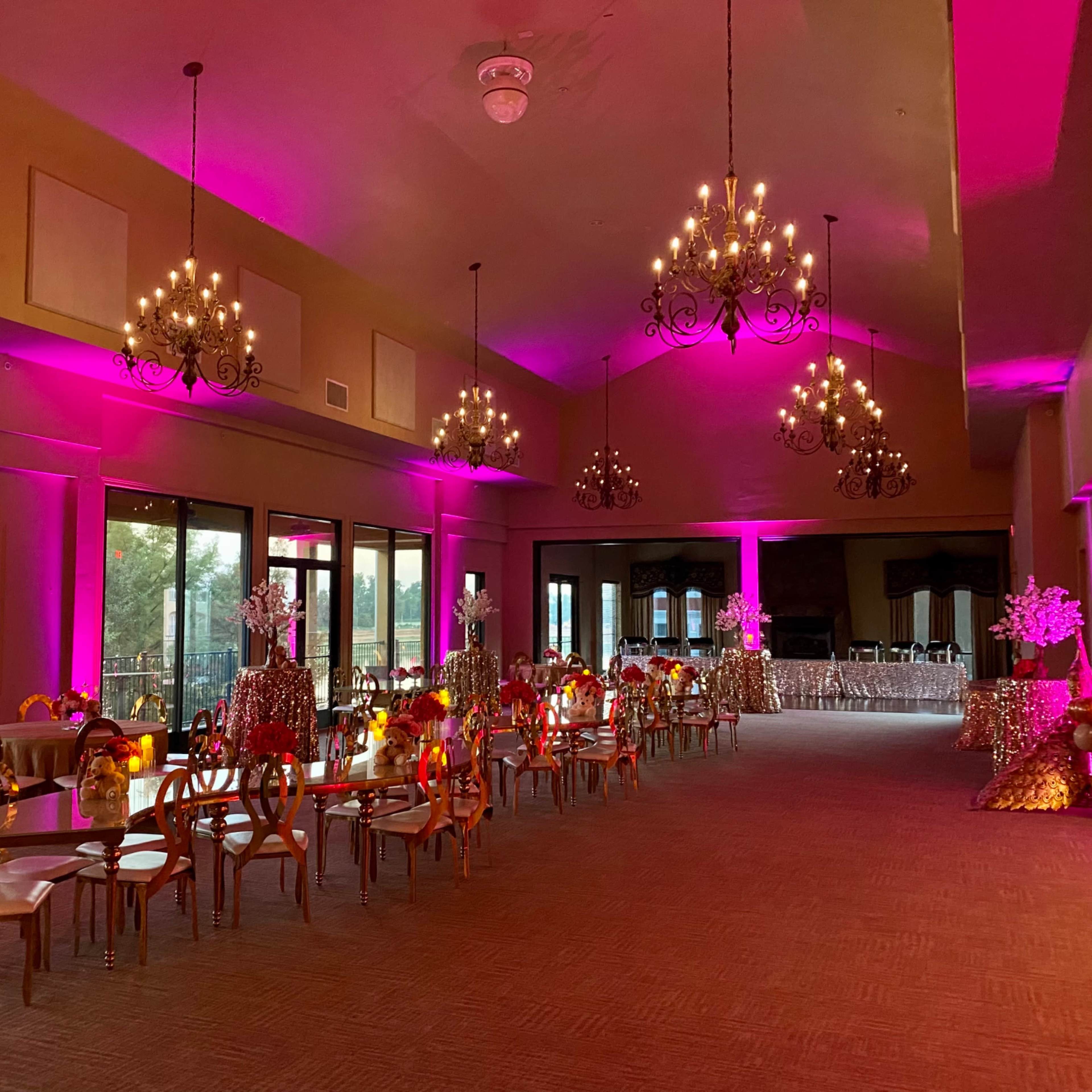 A banquet hall decorated with pink lighting, chandeliers, and ornate tables set up for an event.