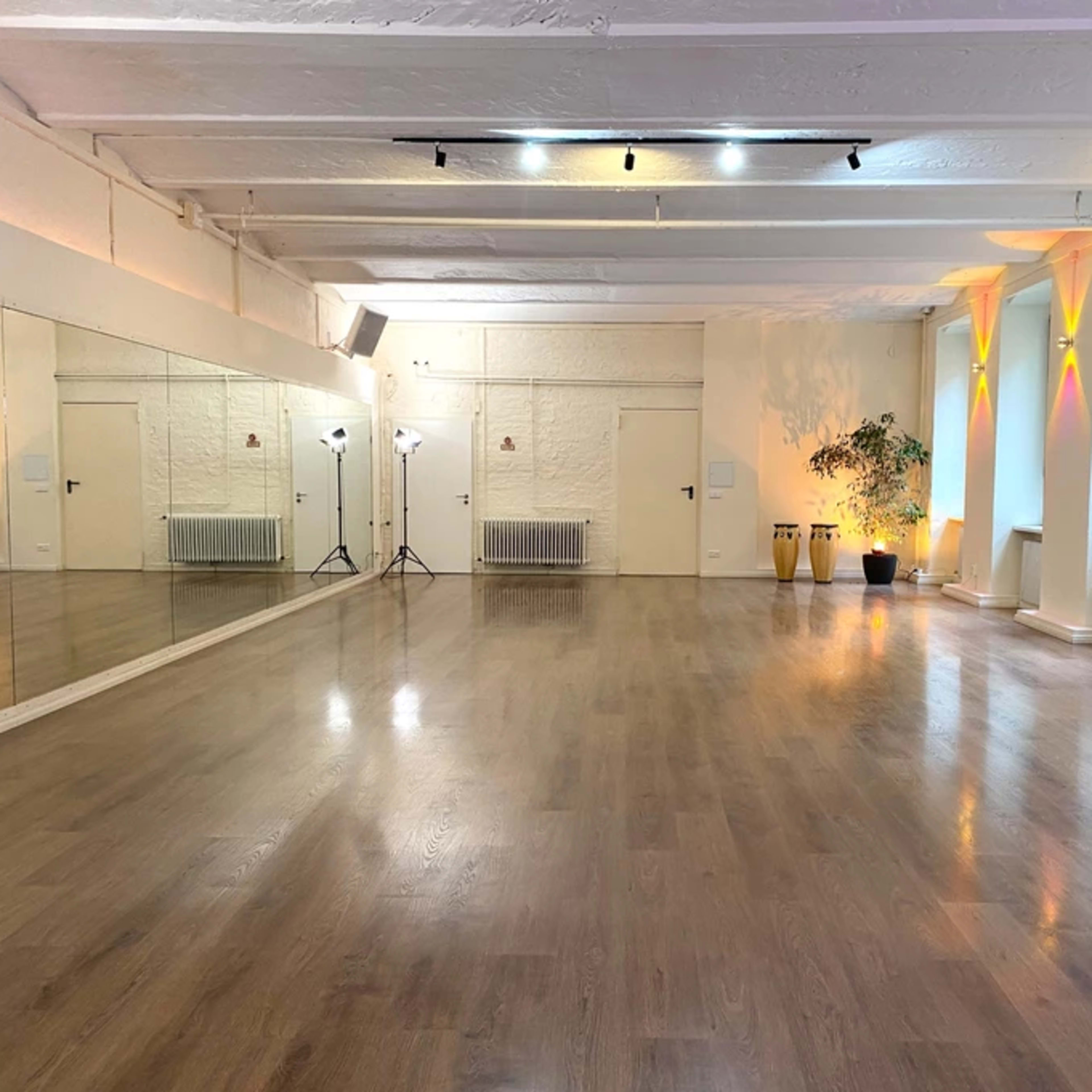 An empty dance studio with wooden floors, white walls, mirrors, and soft lighting.
