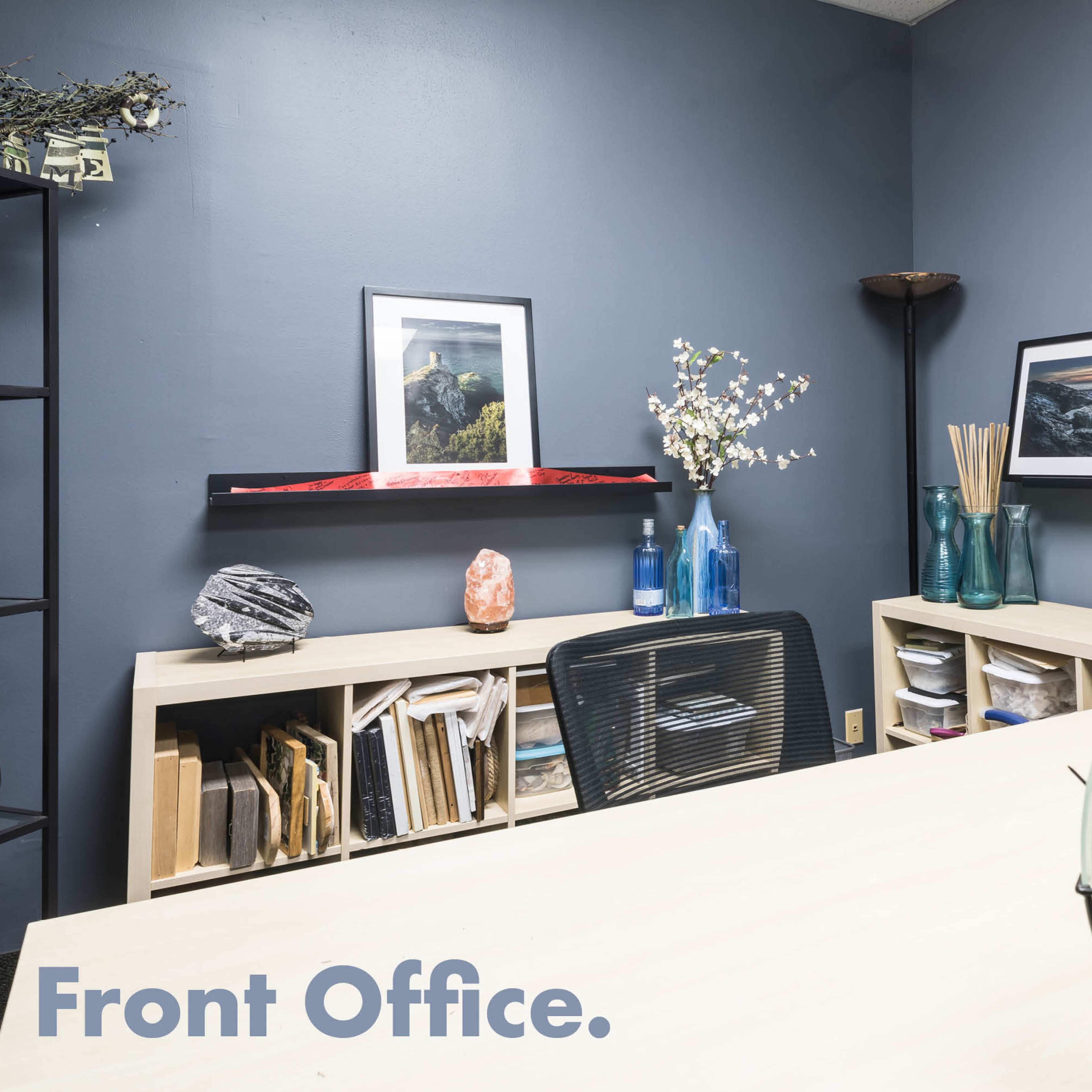 A front office with dark gray walls, modern shelving units filled with books and decorative items, and a wooden desk with a black chair.
