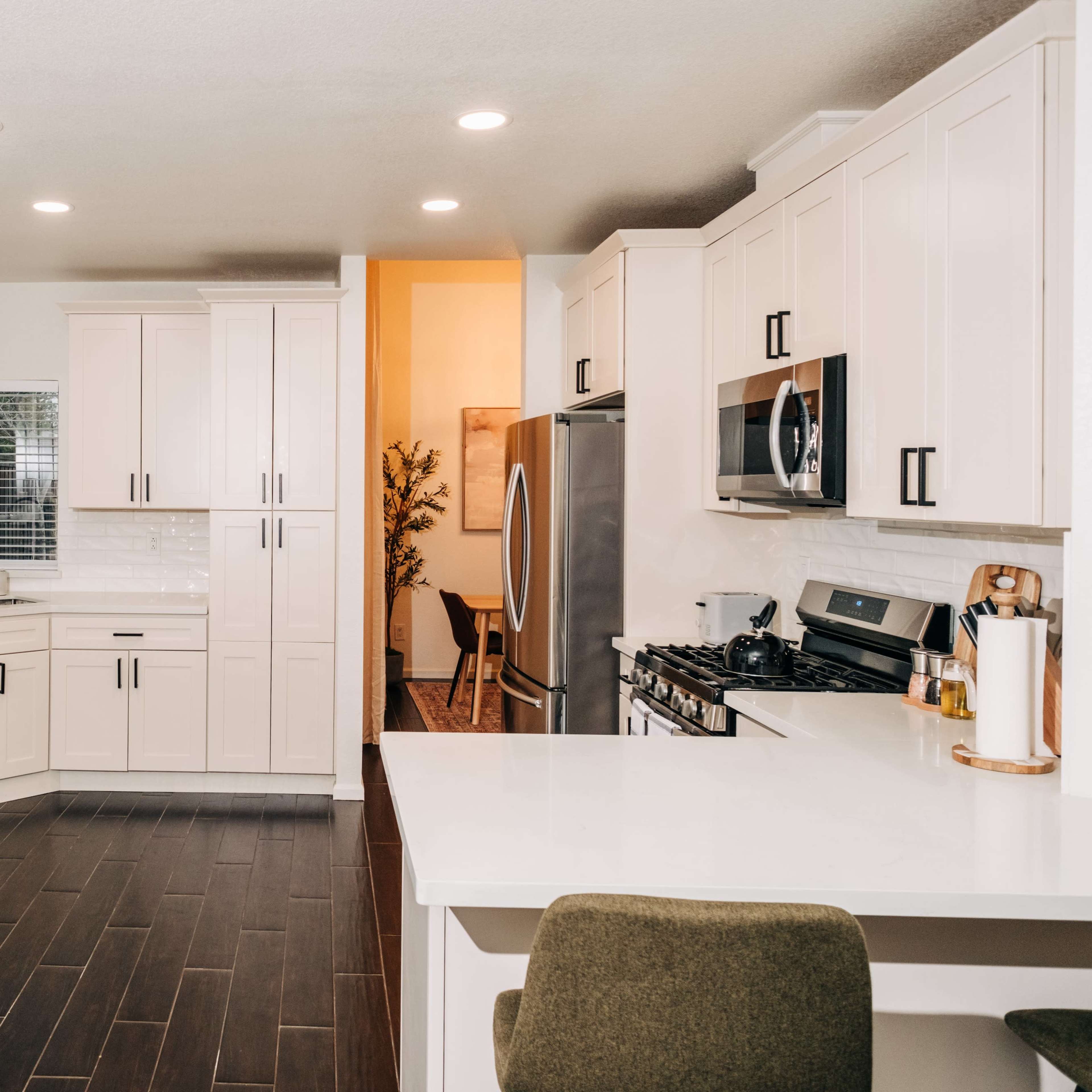 A modern kitchen features white cabinetry, stainless steel appliances, and dark wood flooring.