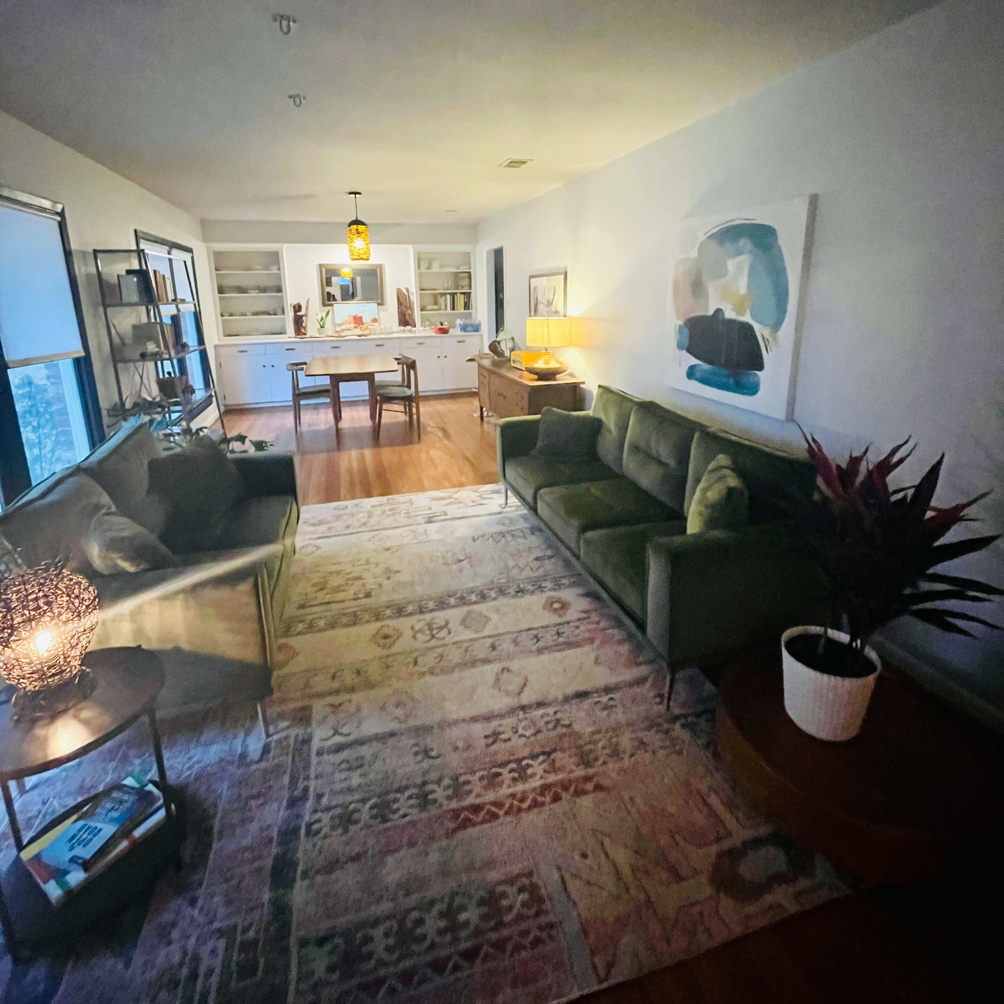 A living room with a green sofa, a patterned rug, a coffee table, and a dining area visible in the background.
