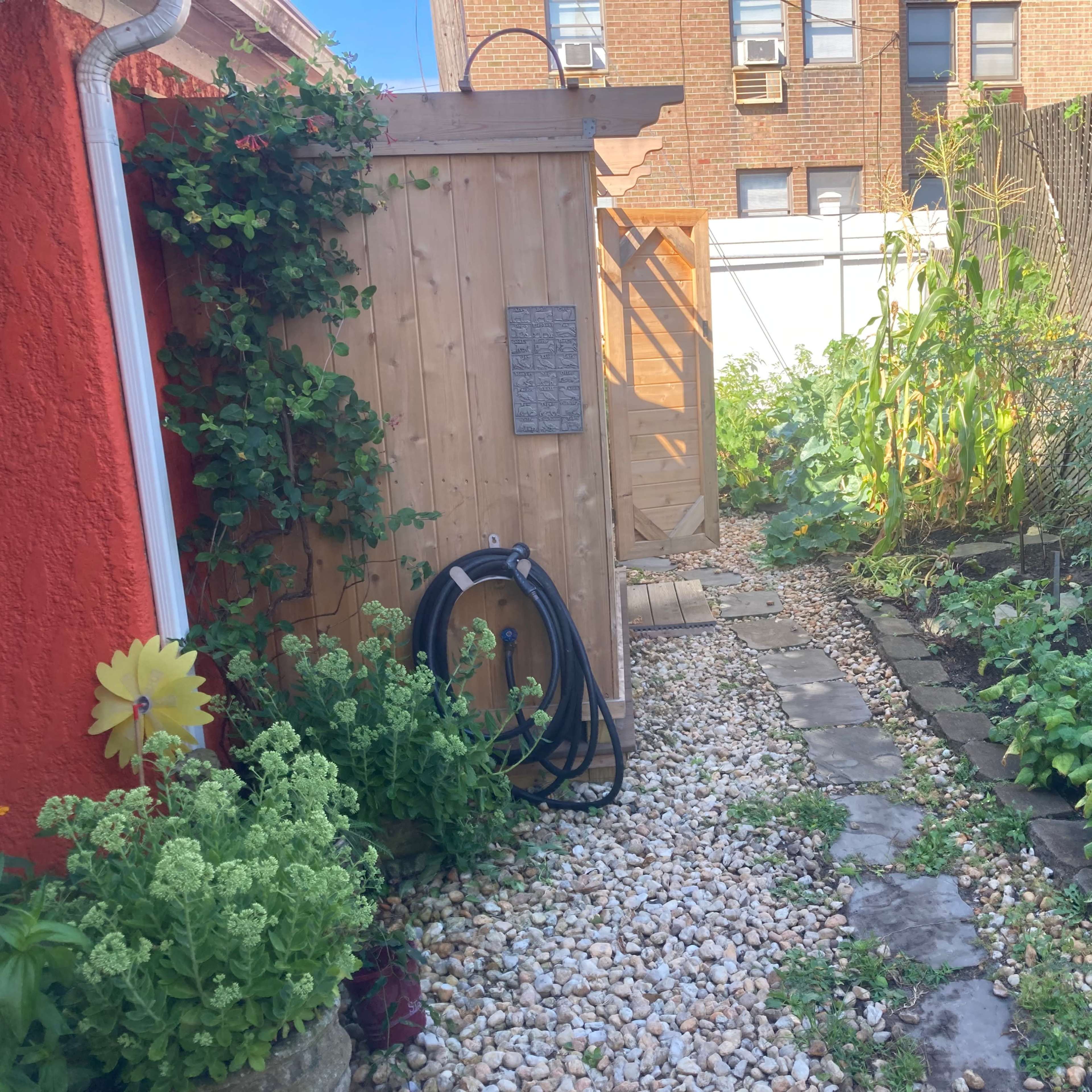 A narrow garden pathway lined with stones and gravel leads to a wooden gate surrounded by plants and greenery.