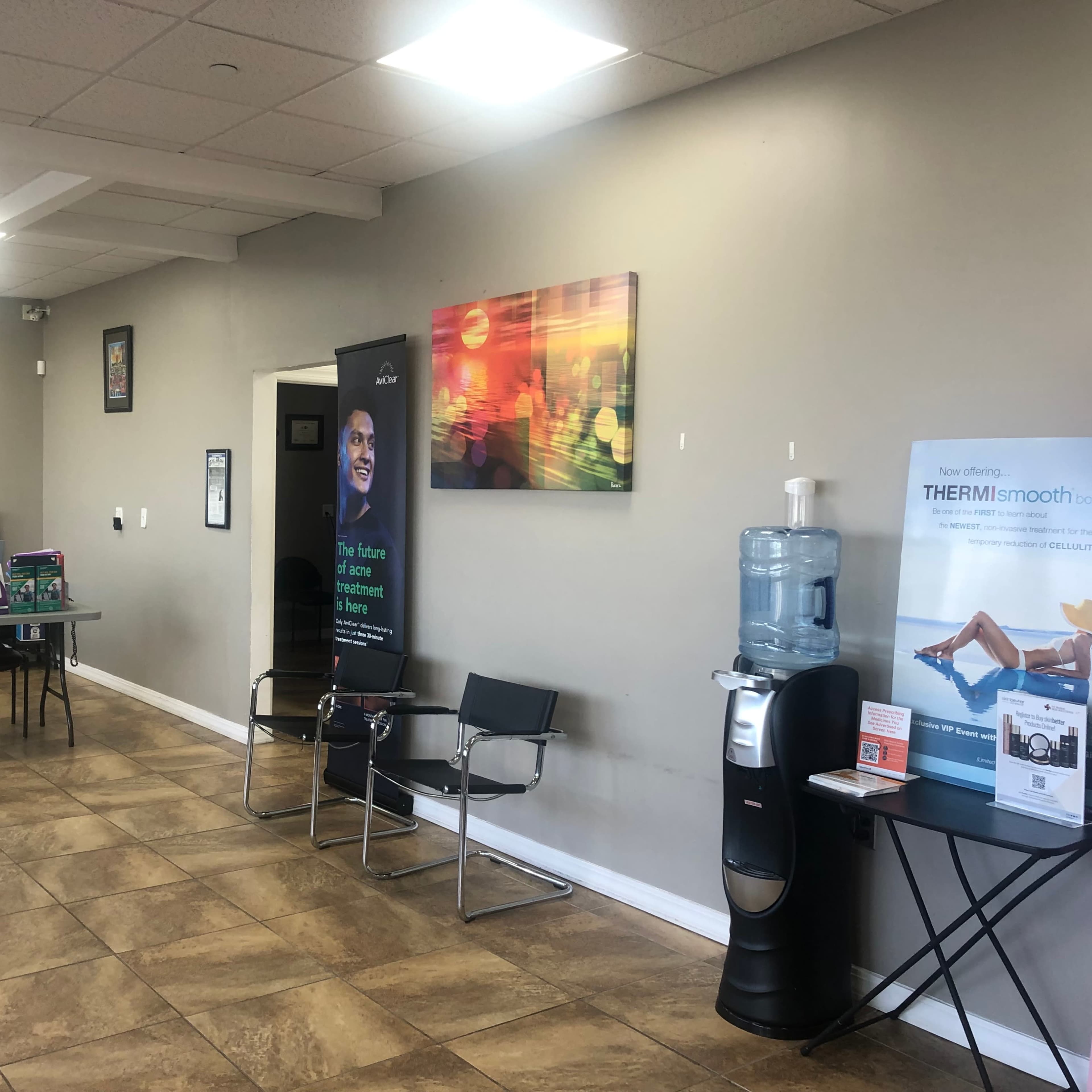 An interior space with a reception area featuring a water cooler, chairs, a table with promotional materials, and colorful artwork on the walls.