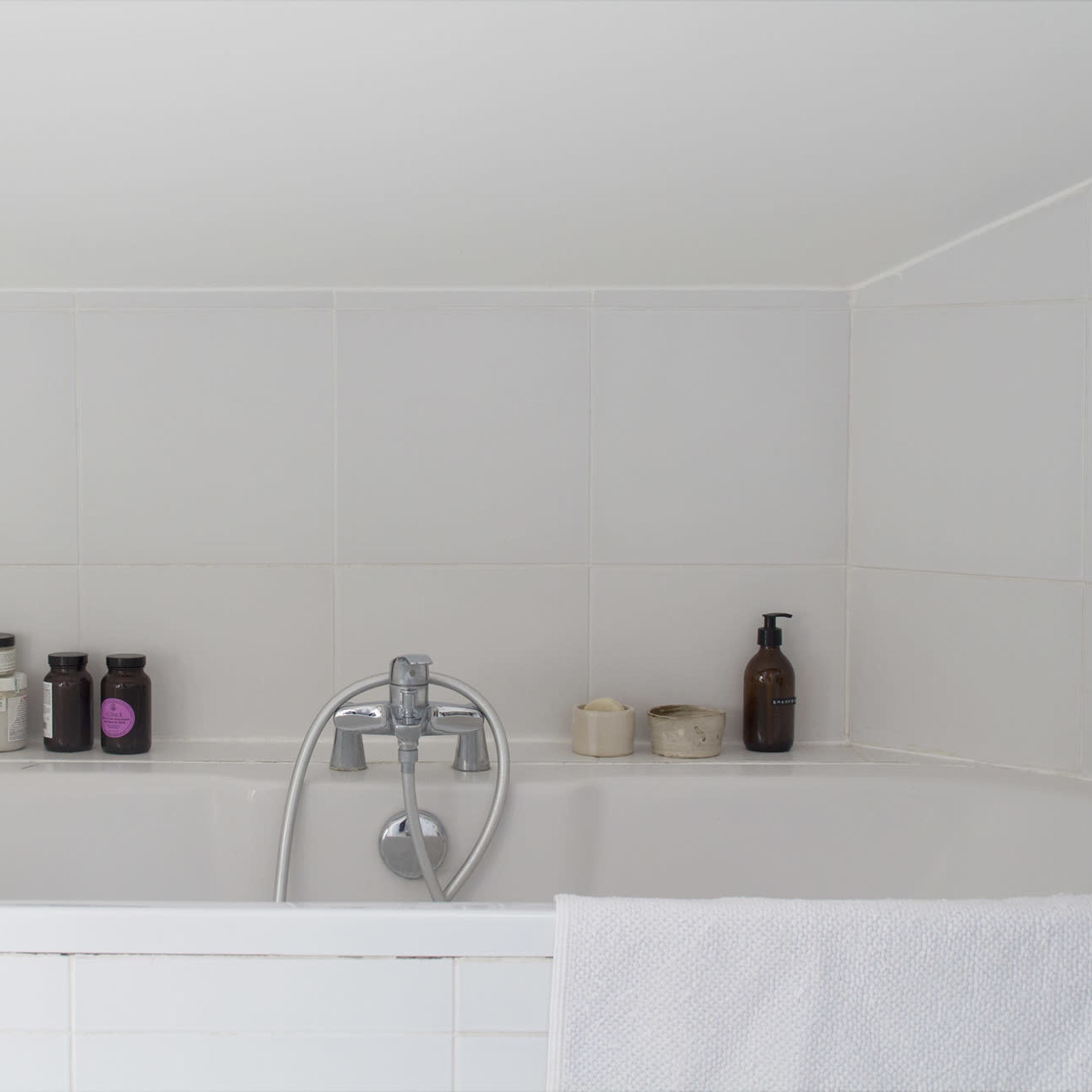 A clean, white bathtub is accompanied by neatly arranged bottles of bath products on the ledge.