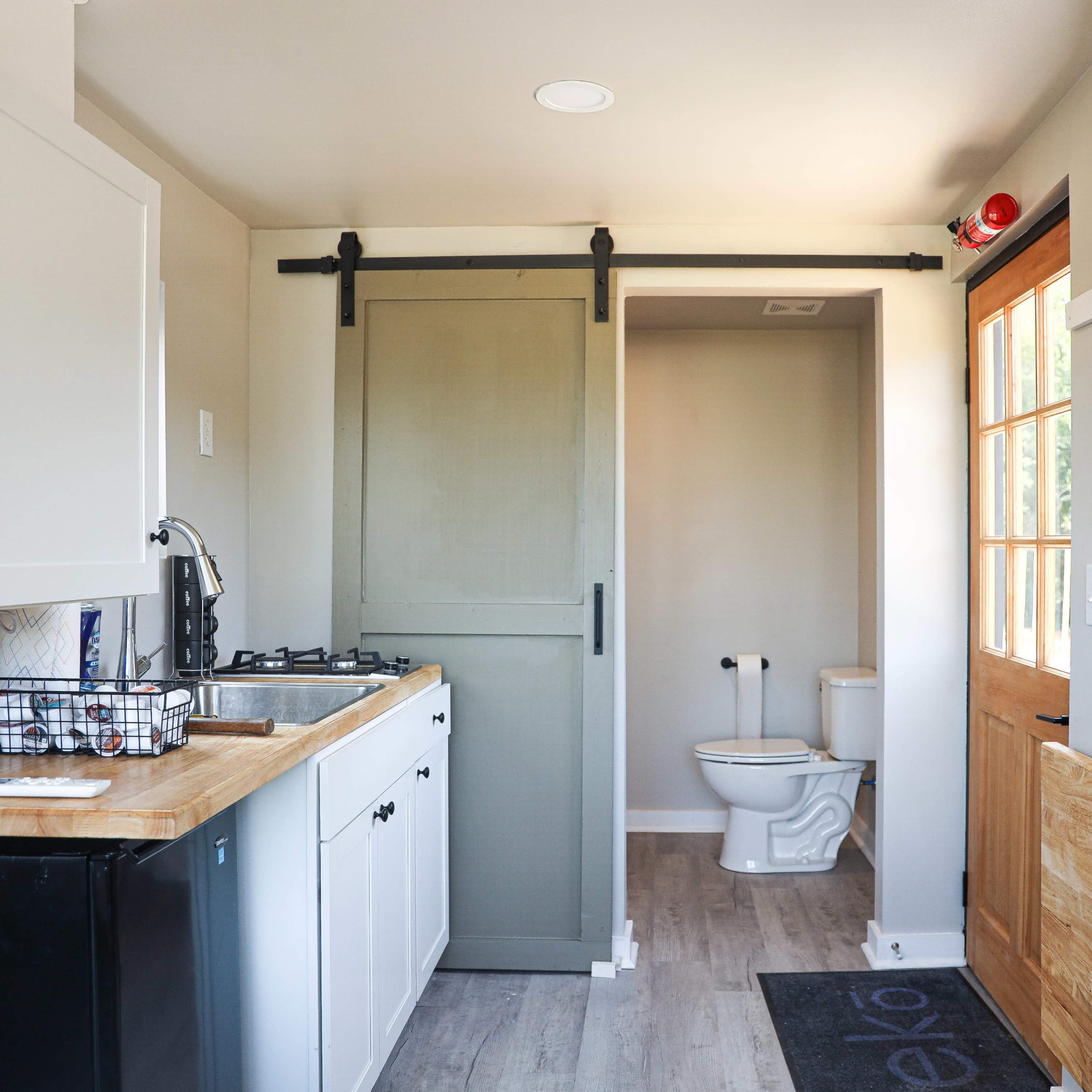 A compact kitchen area featuring a sink, stove, a refrigerator, and a sliding barn door that leads to a bathroom with a toilet.