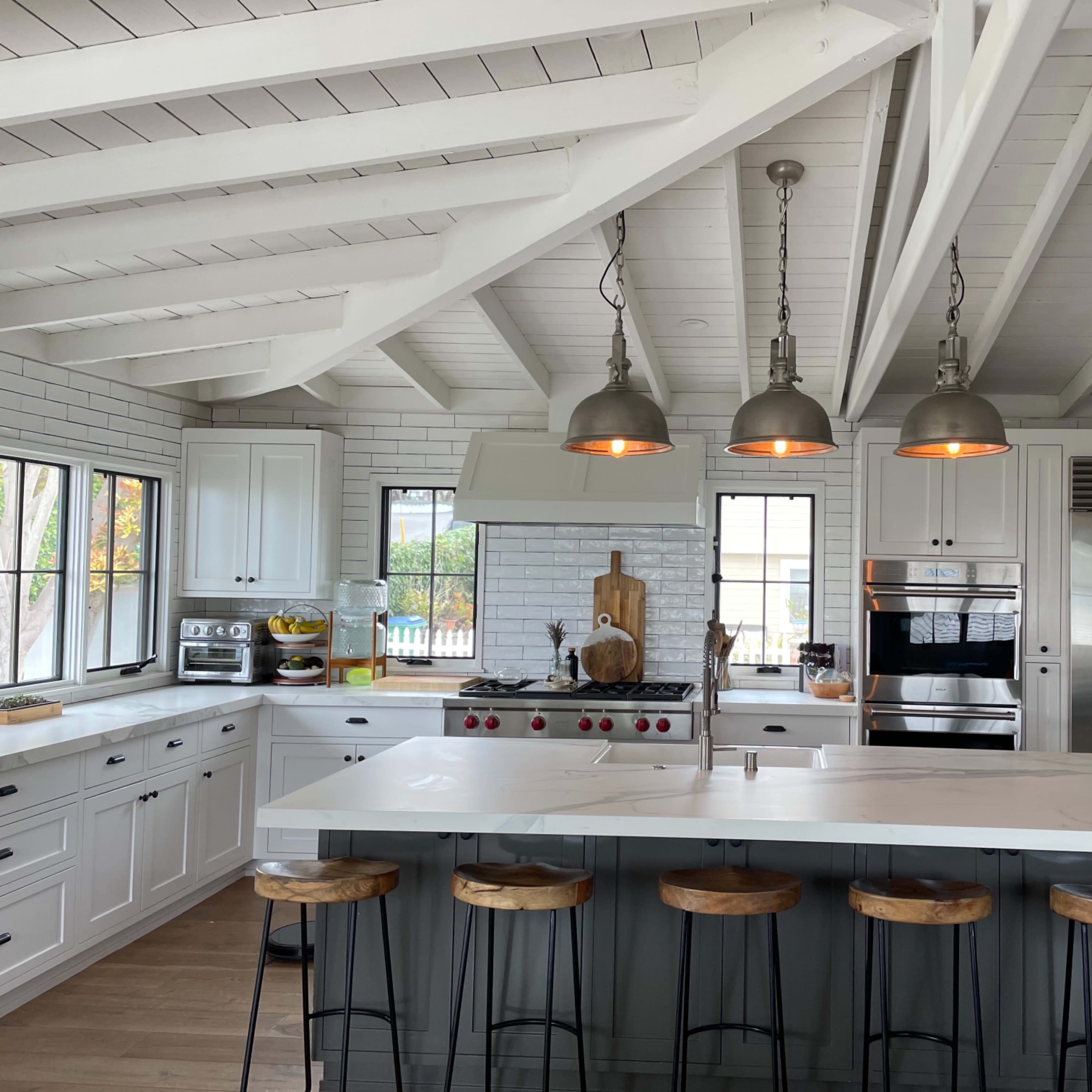 A modern kitchen with a spacious island, white cabinetry, and stainless steel appliances under exposed wooden beams.