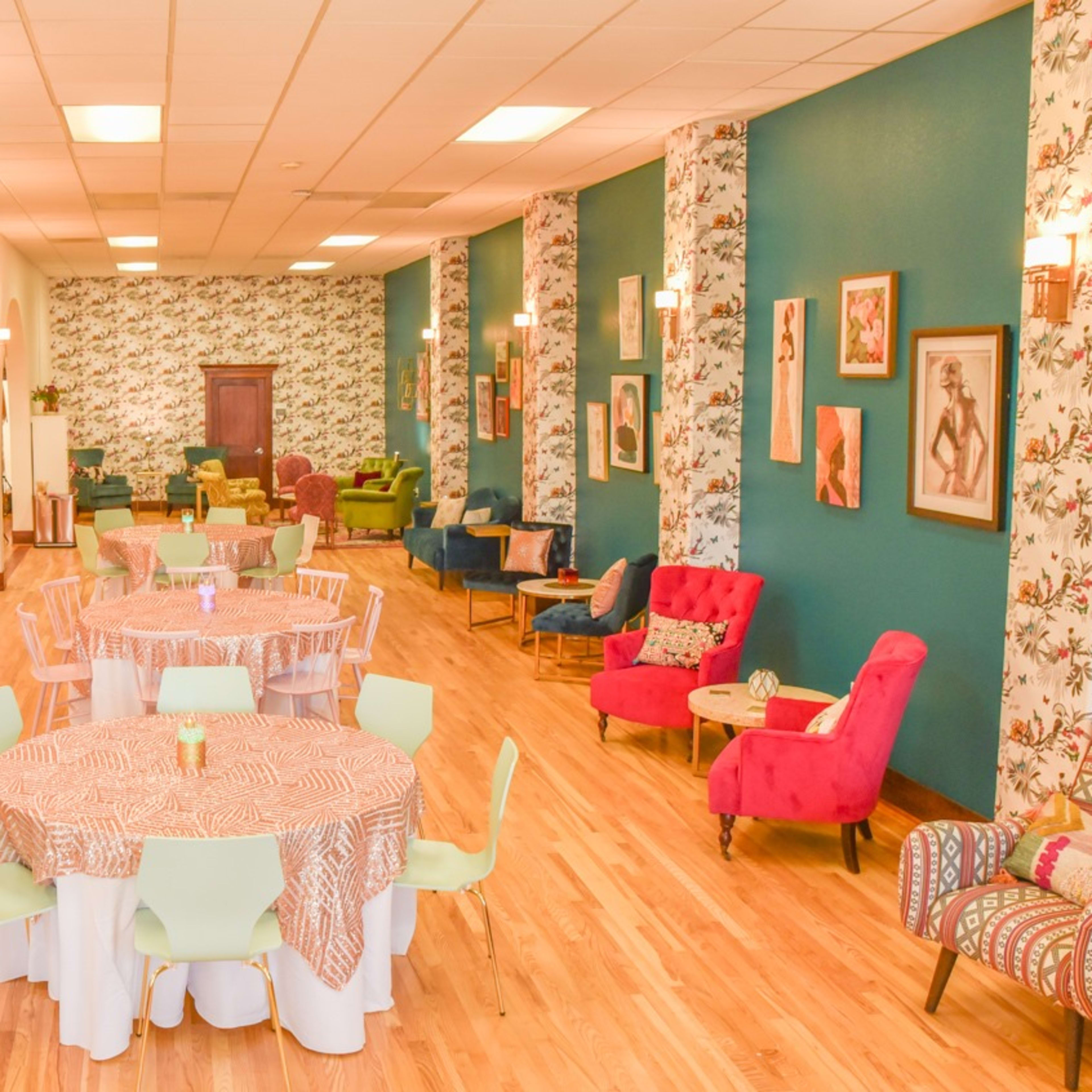 A spacious event hall with colorful furniture, floral wallpaper, and tables set with patterned tablecloths.