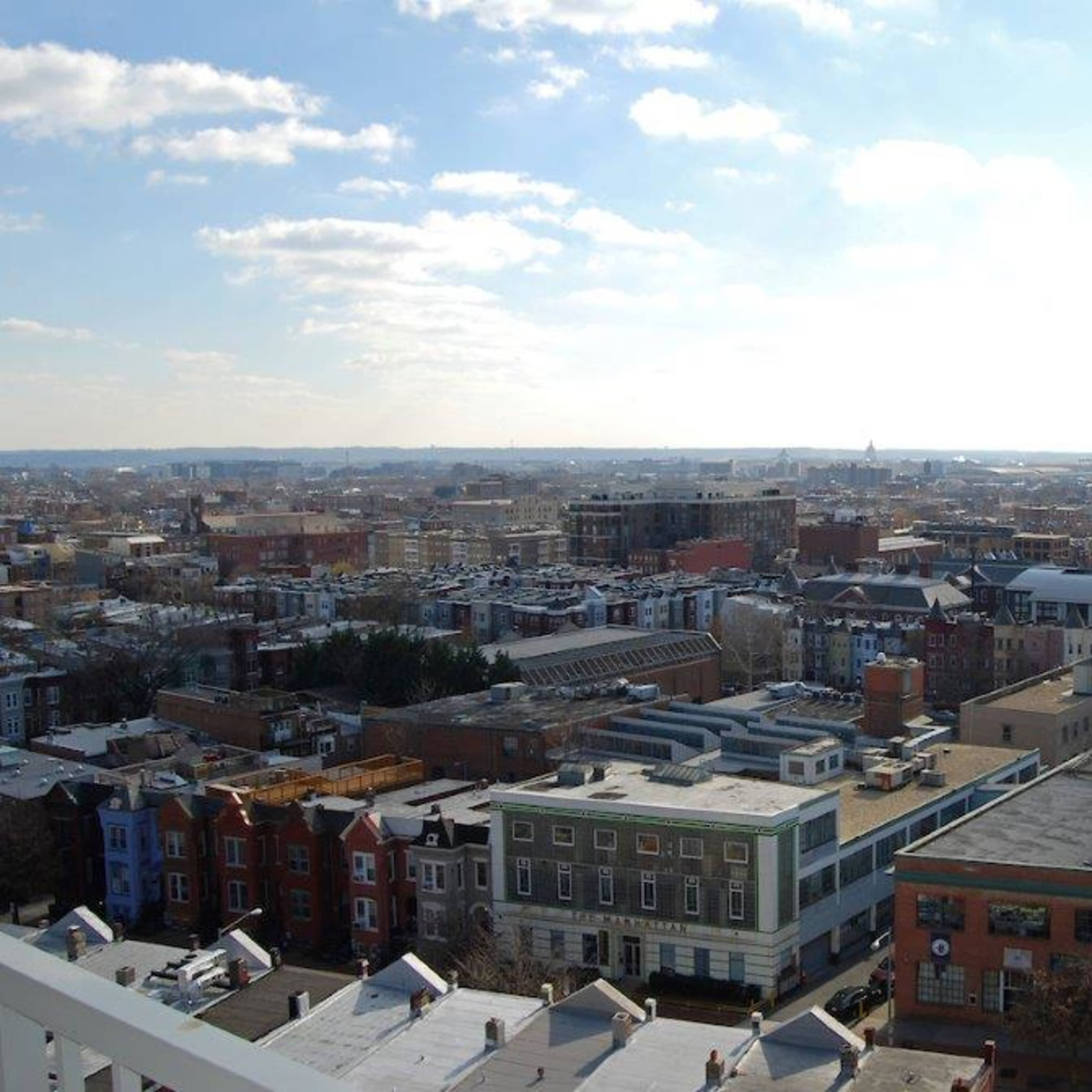 A panoramic view of a city skyline with a mix of residential and commercial buildings under a partly cloudy sky.