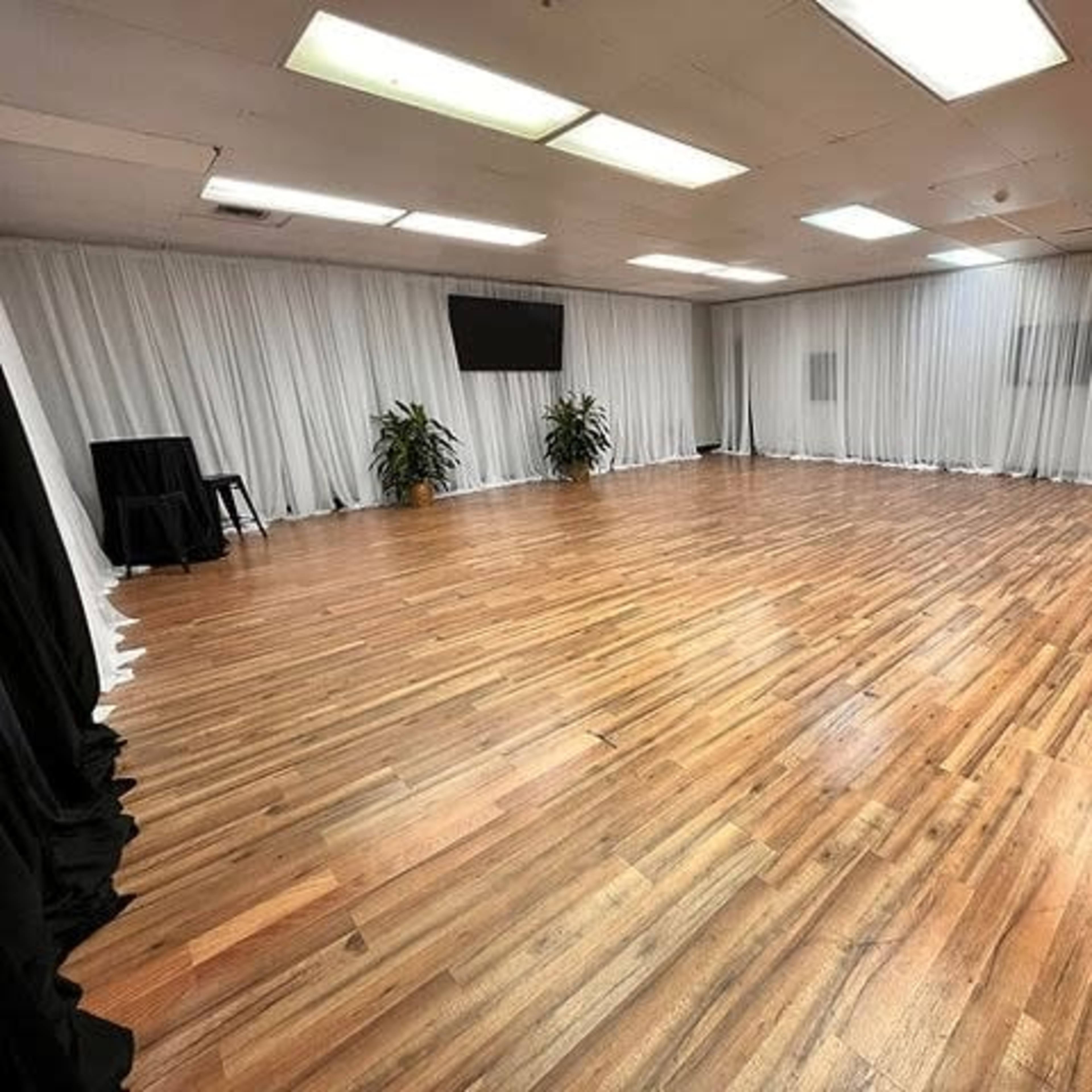 A spacious indoor room with wooden flooring, white drapes along the walls, and a large, empty area.
