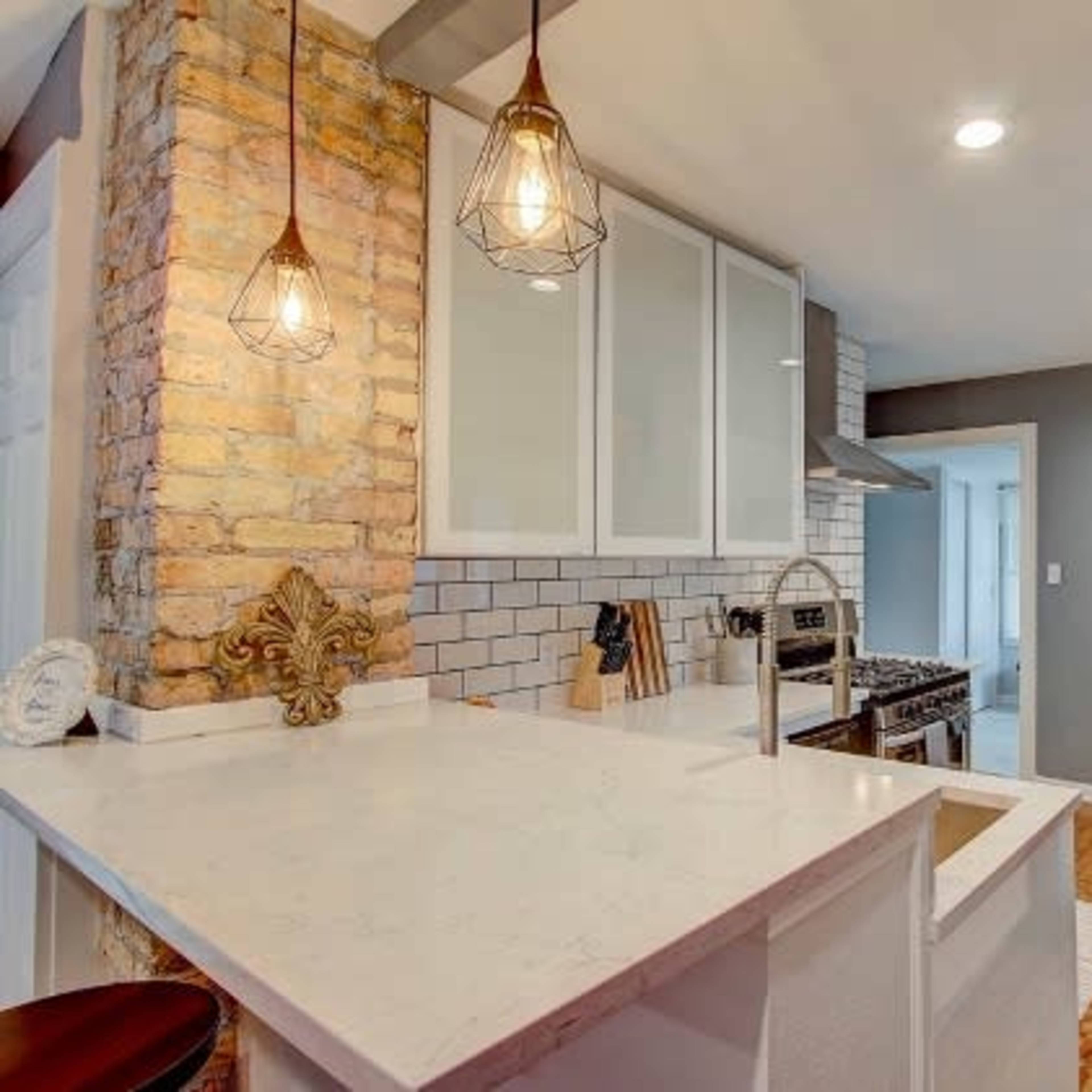 A modern kitchen featuring a central island with a white countertop, pendant lights, and stainless steel appliances against a backdrop of gray and white walls.