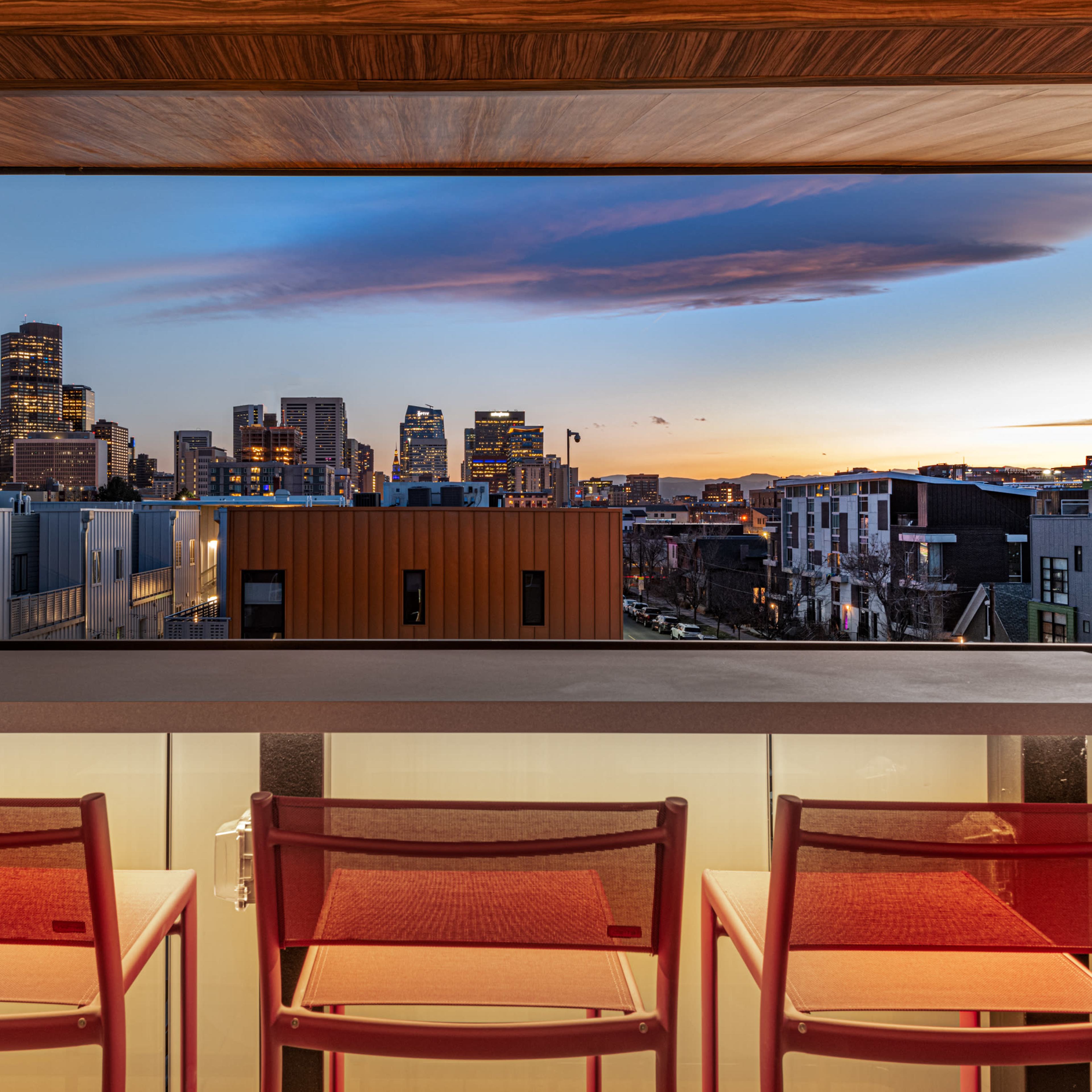 A rooftop terrace with several tables and high chairs overlooking a cityscape under a partly cloudy sky.