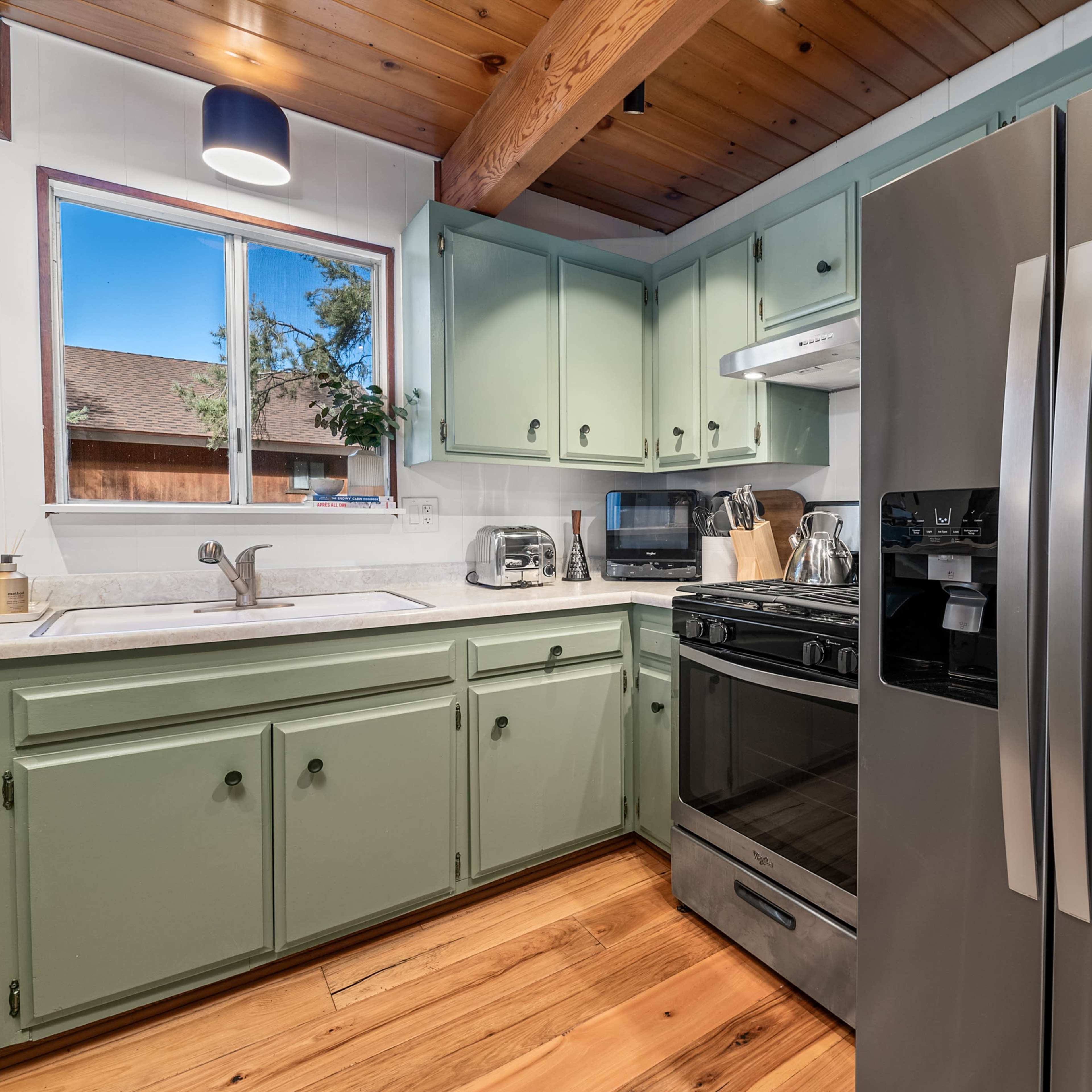 A kitchen with green-painted cabinets, a stainless steel refrigerator, and wooden flooring.
