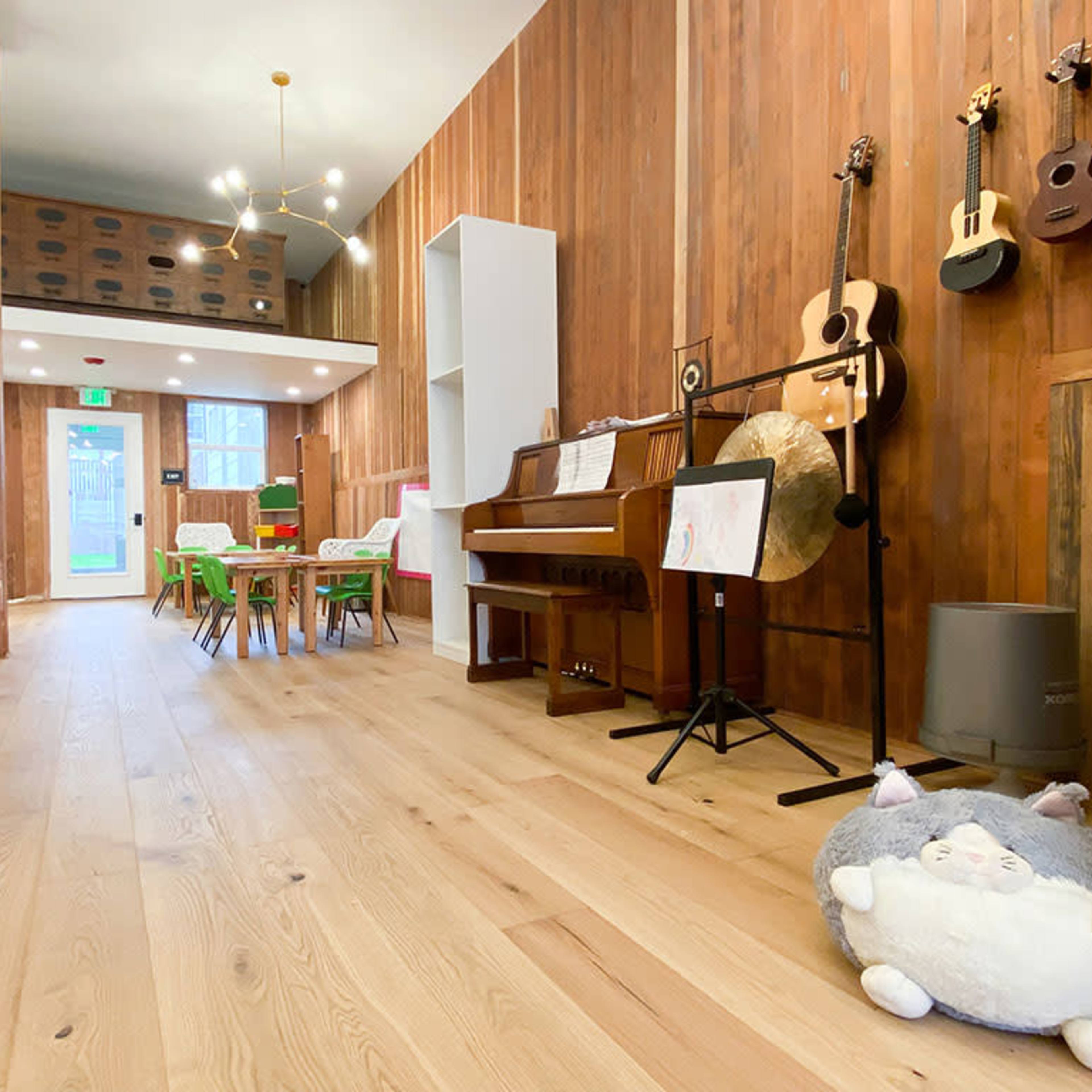 A spacious room with wooden walls, a piano, musical instruments on display, and tables with chairs arranged for a gathering.