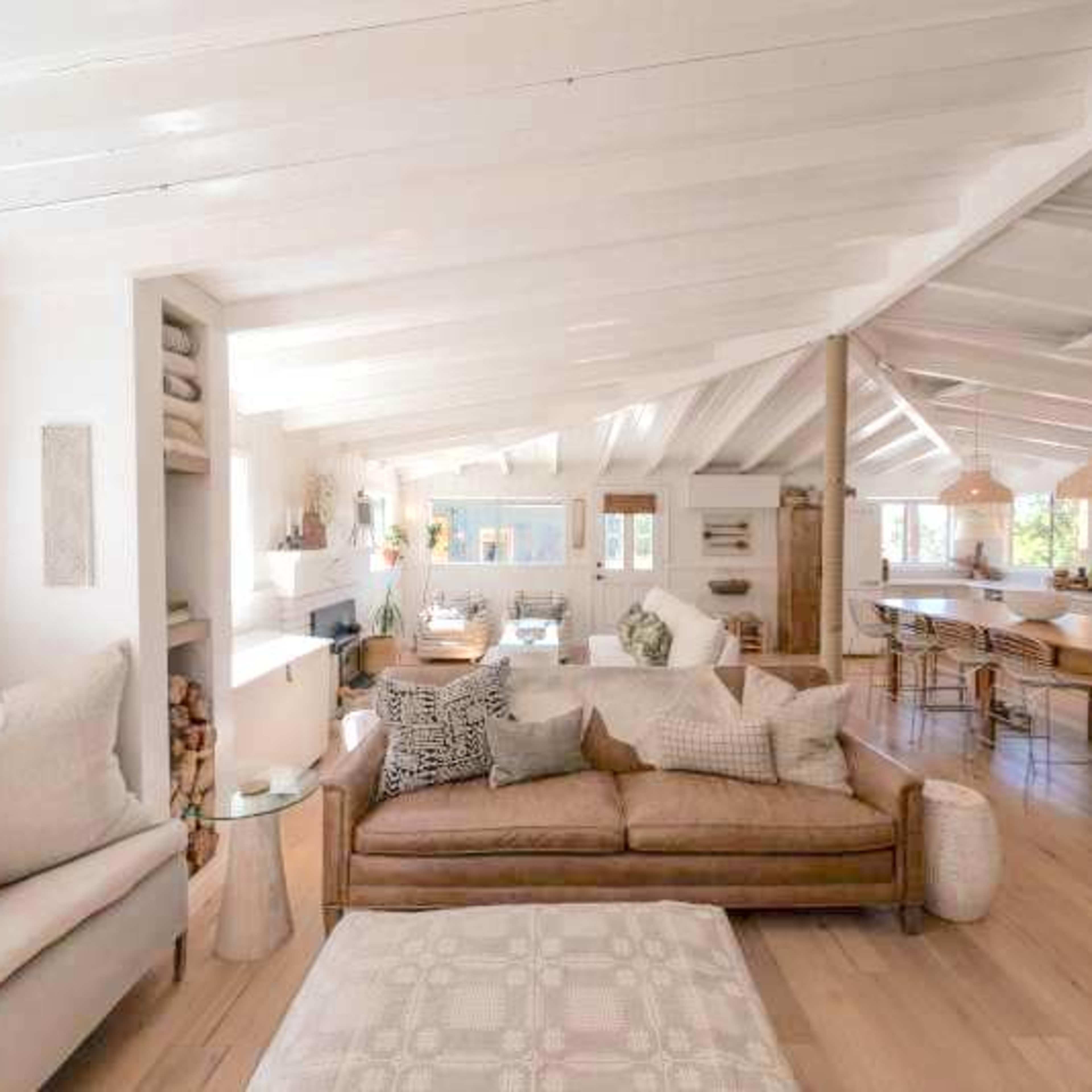 The spacious interior features a living area with a light-colored sofa, wooden floors, and a kitchen bar area.