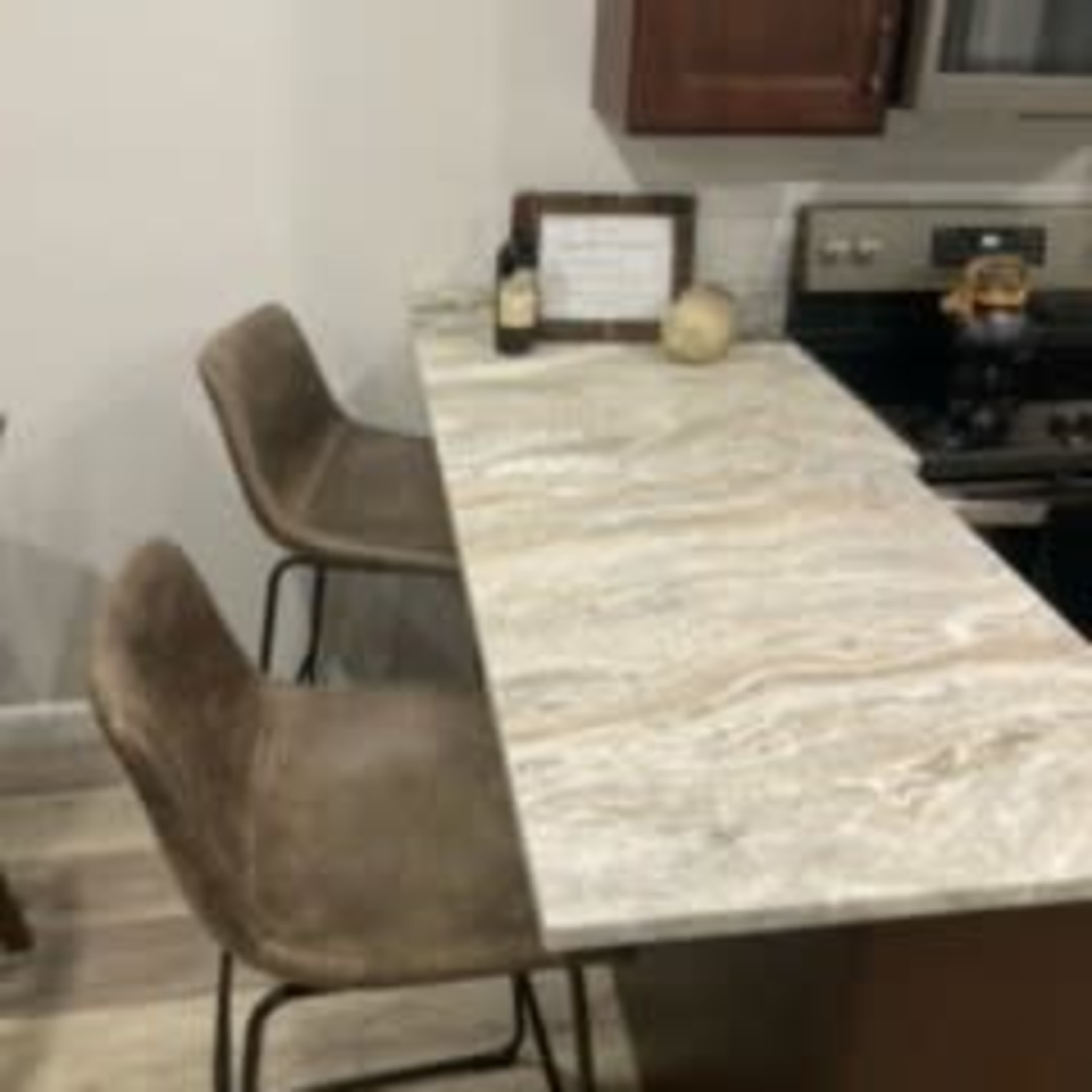 A kitchen bar area with two upholstered stools and a countertop made of patterned stone.
