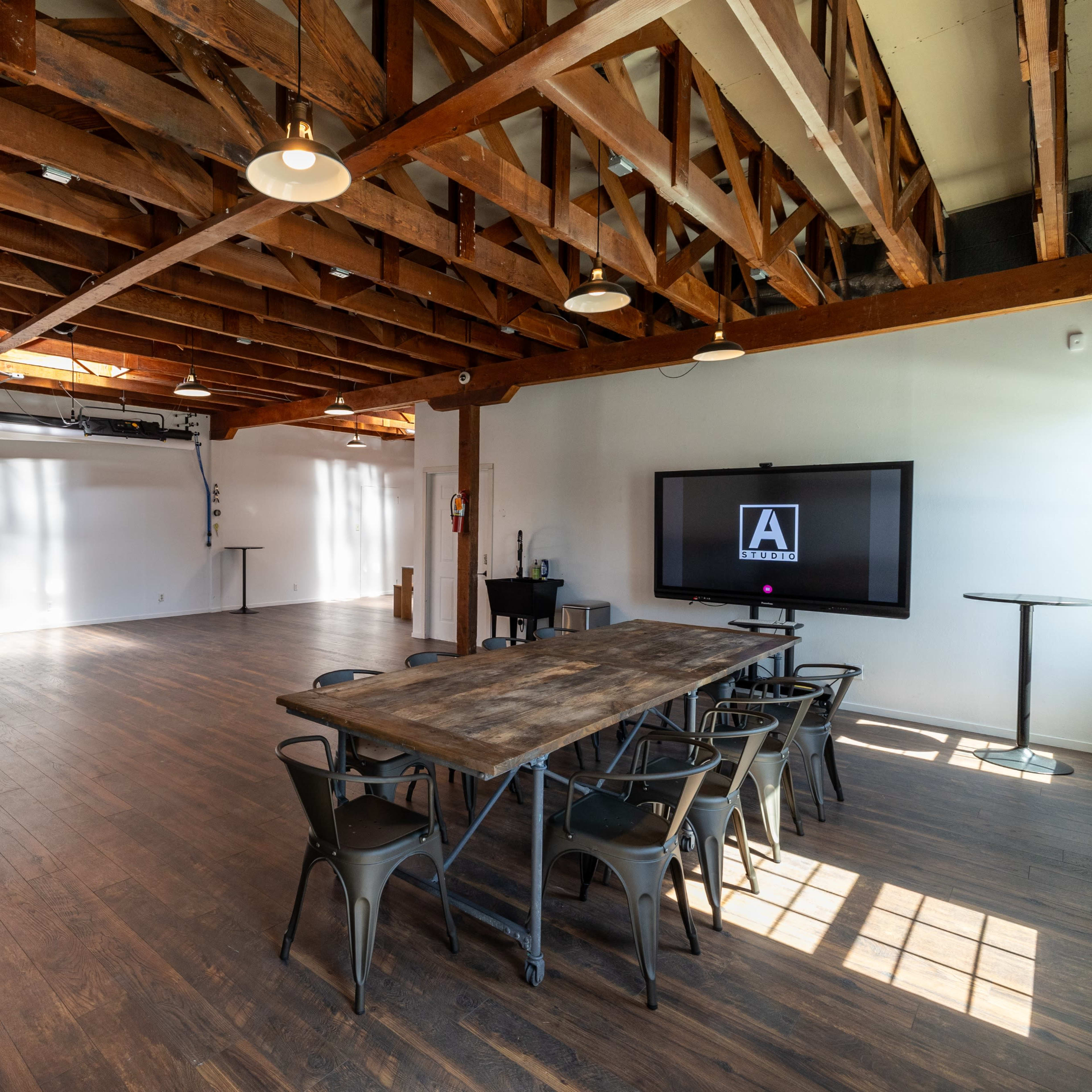 An empty meeting room with wooden beams, a large television screen on one wall, a long wooden table, and black chairs arranged around it.