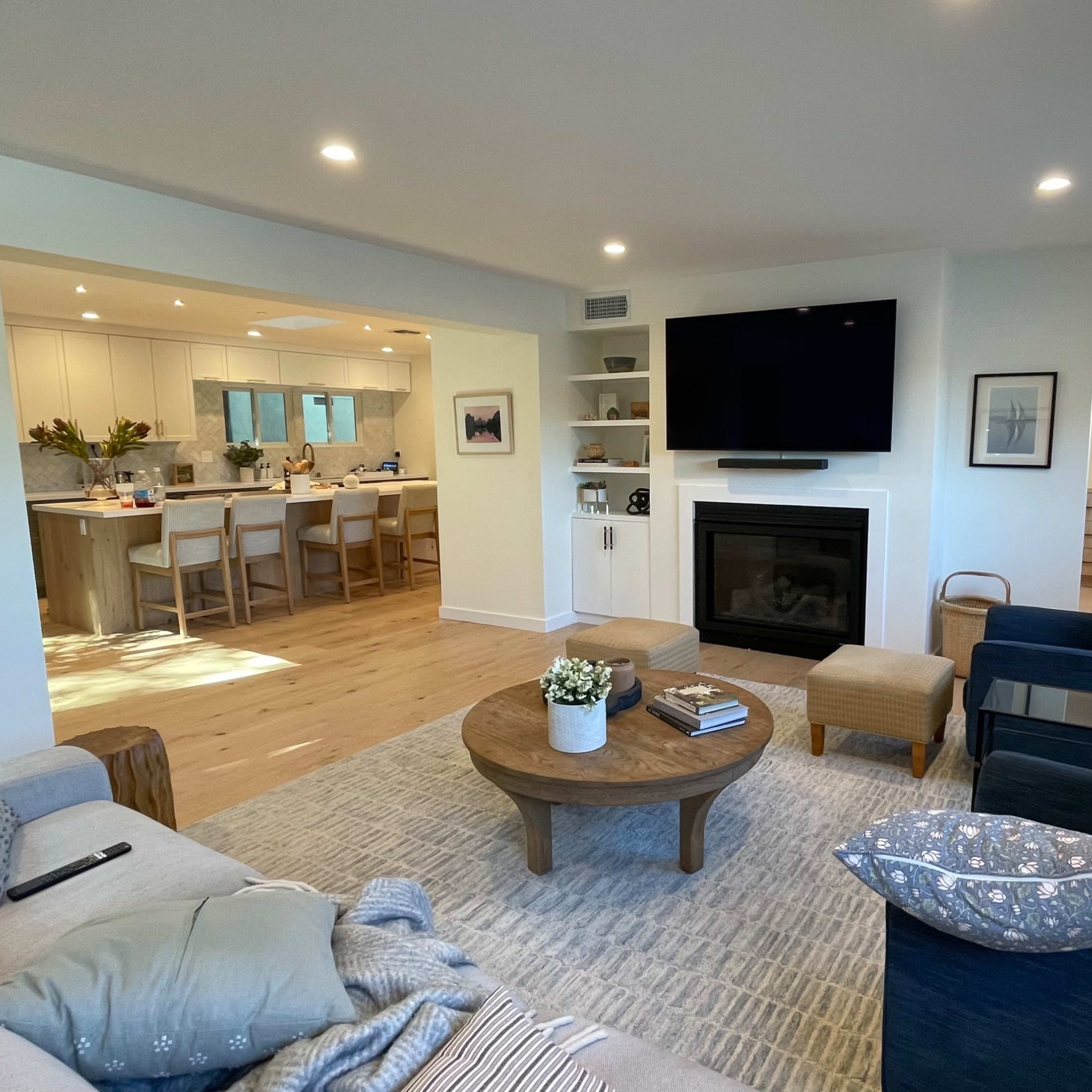 A modern living room with a fireplace, a coffee table, and a view into a bright kitchen area.