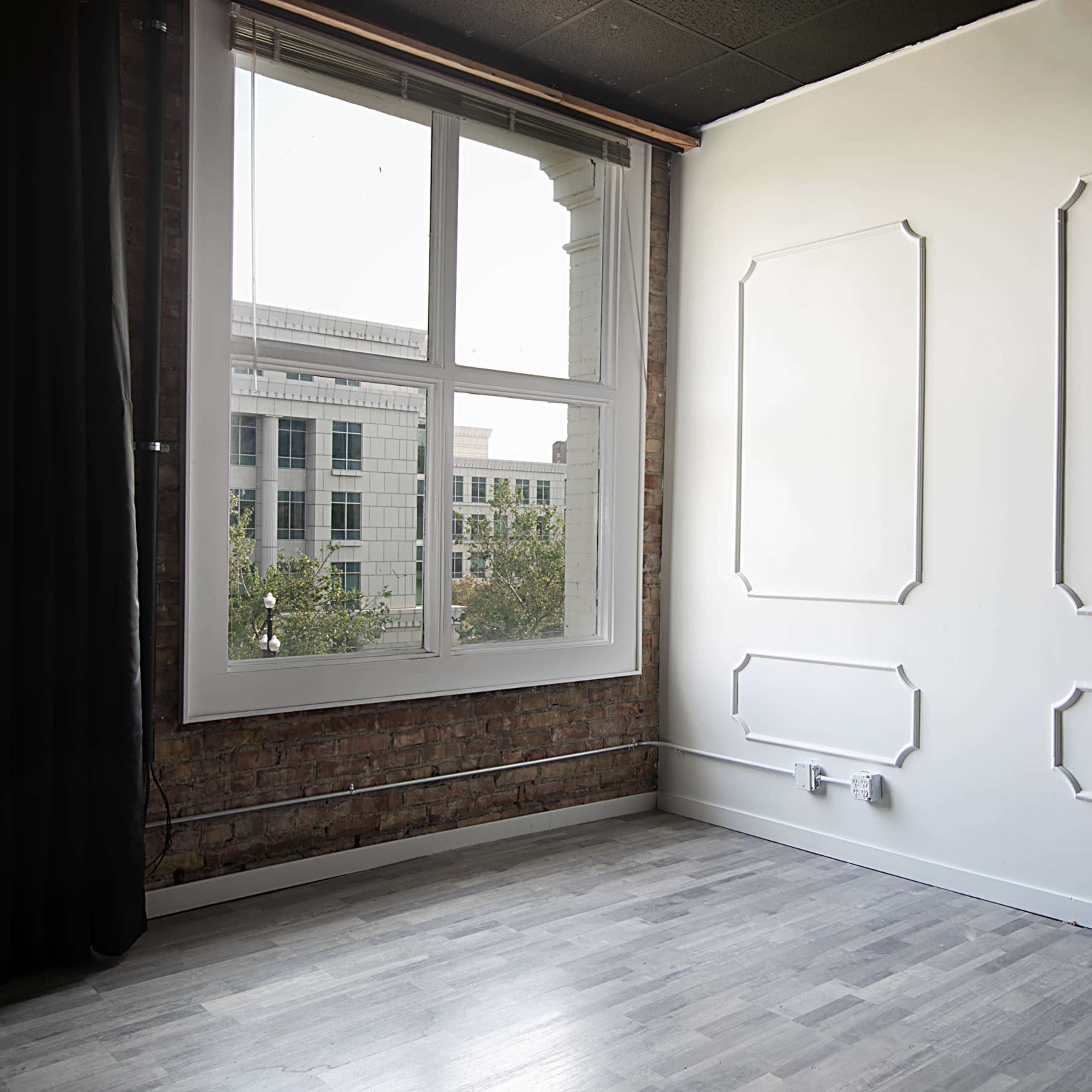 An empty room with a large window, exposed brick wall, and two framed wall panels on a white wall.