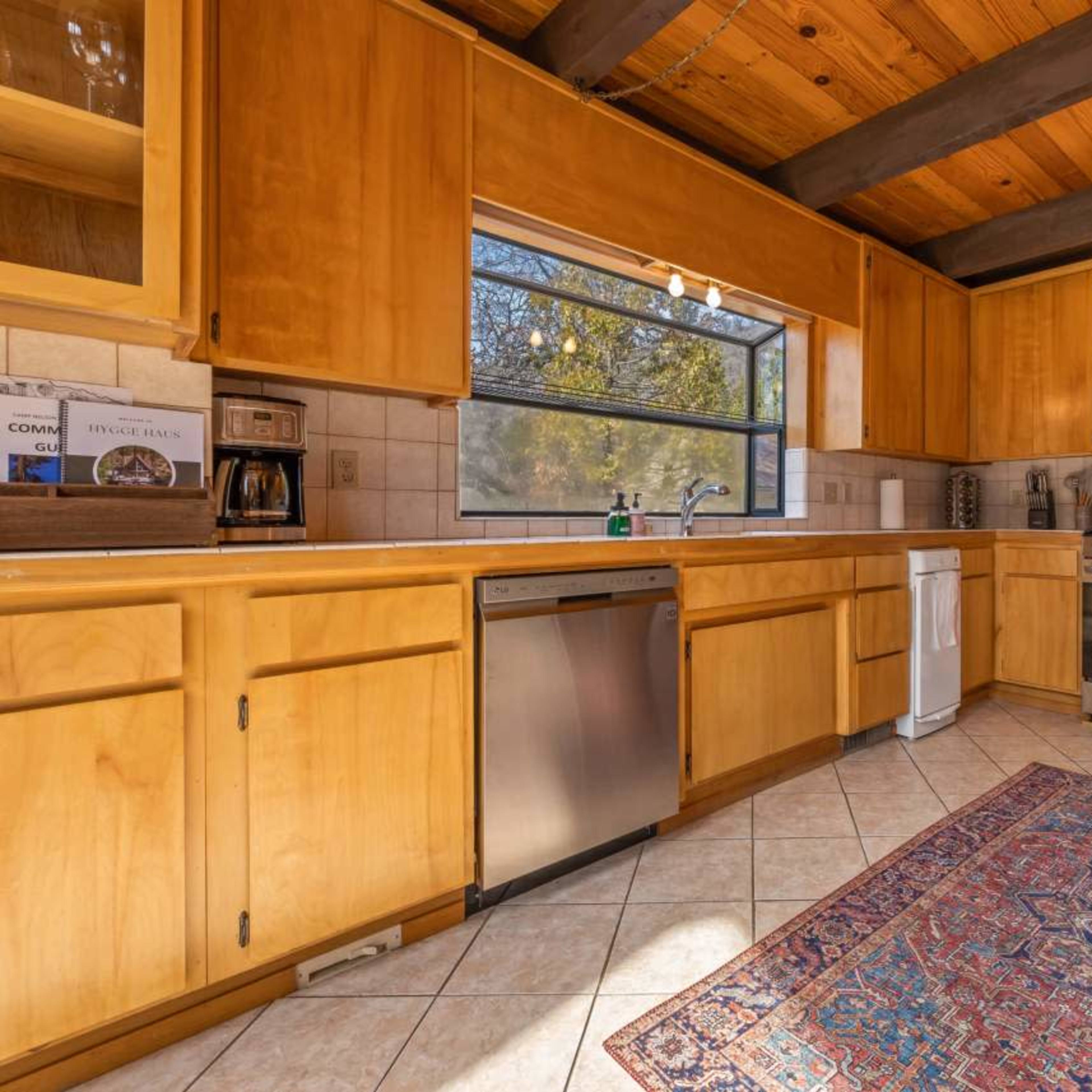 A kitchen with wooden cabinetry, a stainless steel stove, and a patterned rug on the tiled floor.